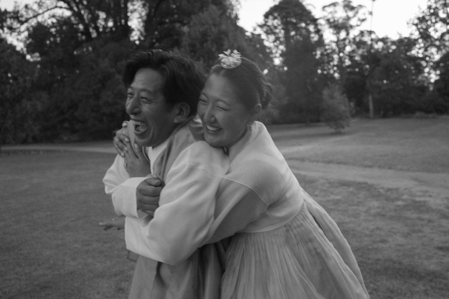 Two people share a joyful embrace and laugh together in a black and white outdoor photo.