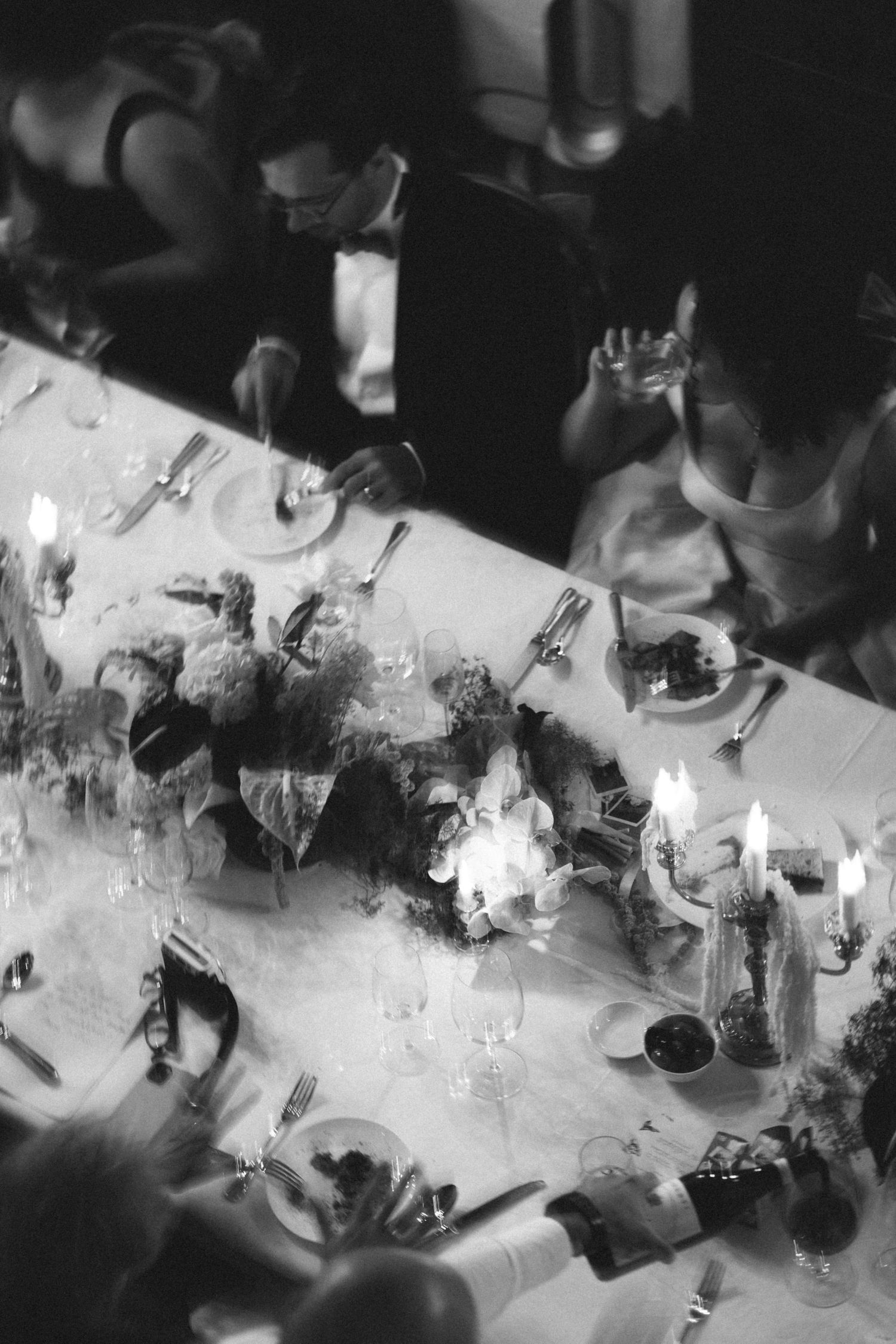 Black and white aerial view of people gathered around tables in a dimly lit room during a social event.