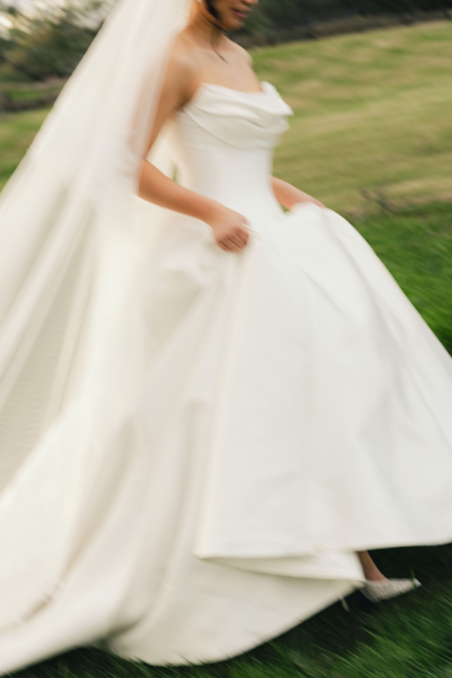 Flowing white wedding dress swirling in motion against green grass background.