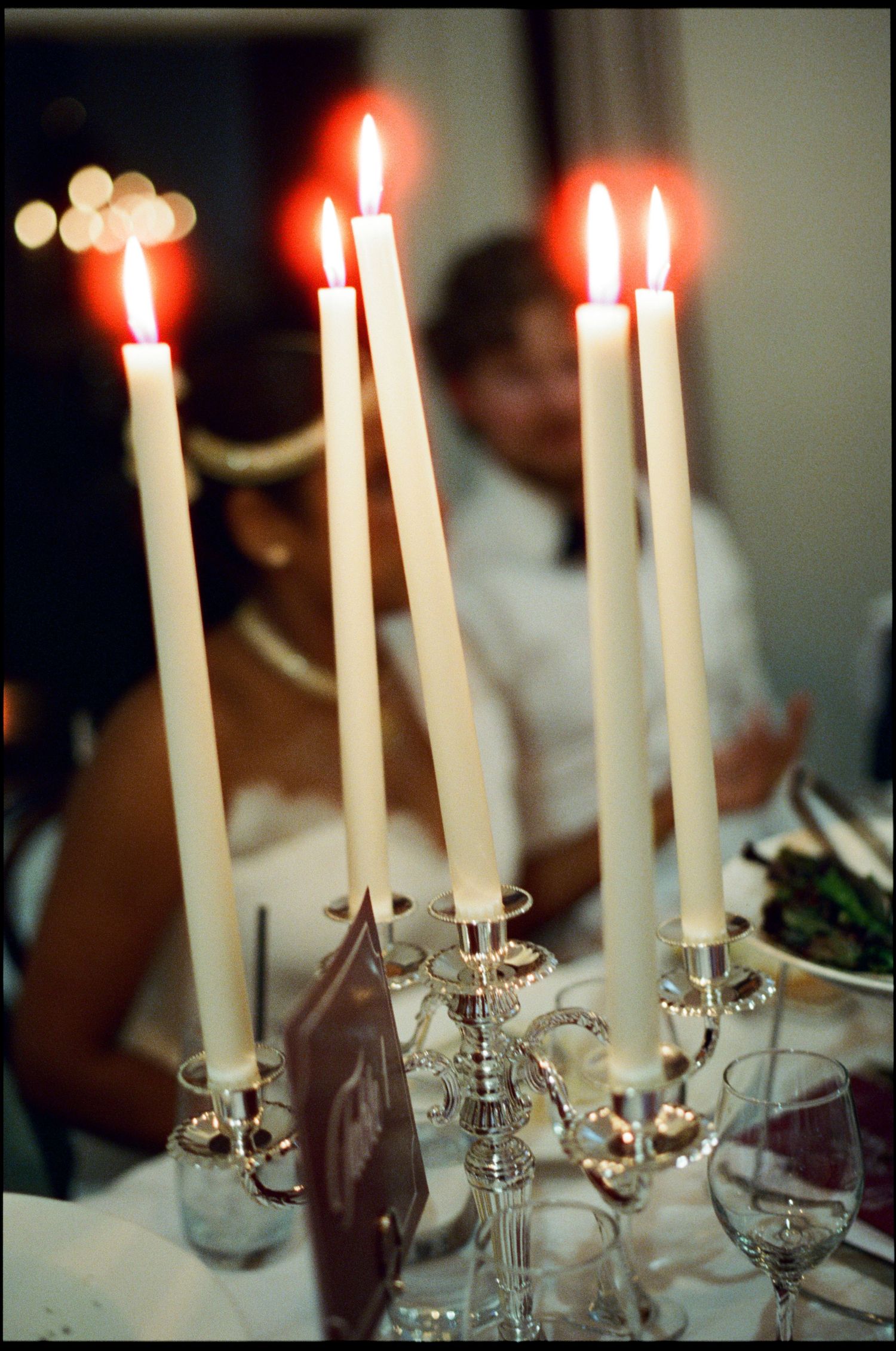 Elegant silver candelabra with five lit white taper candles at a formal dinner party setting.