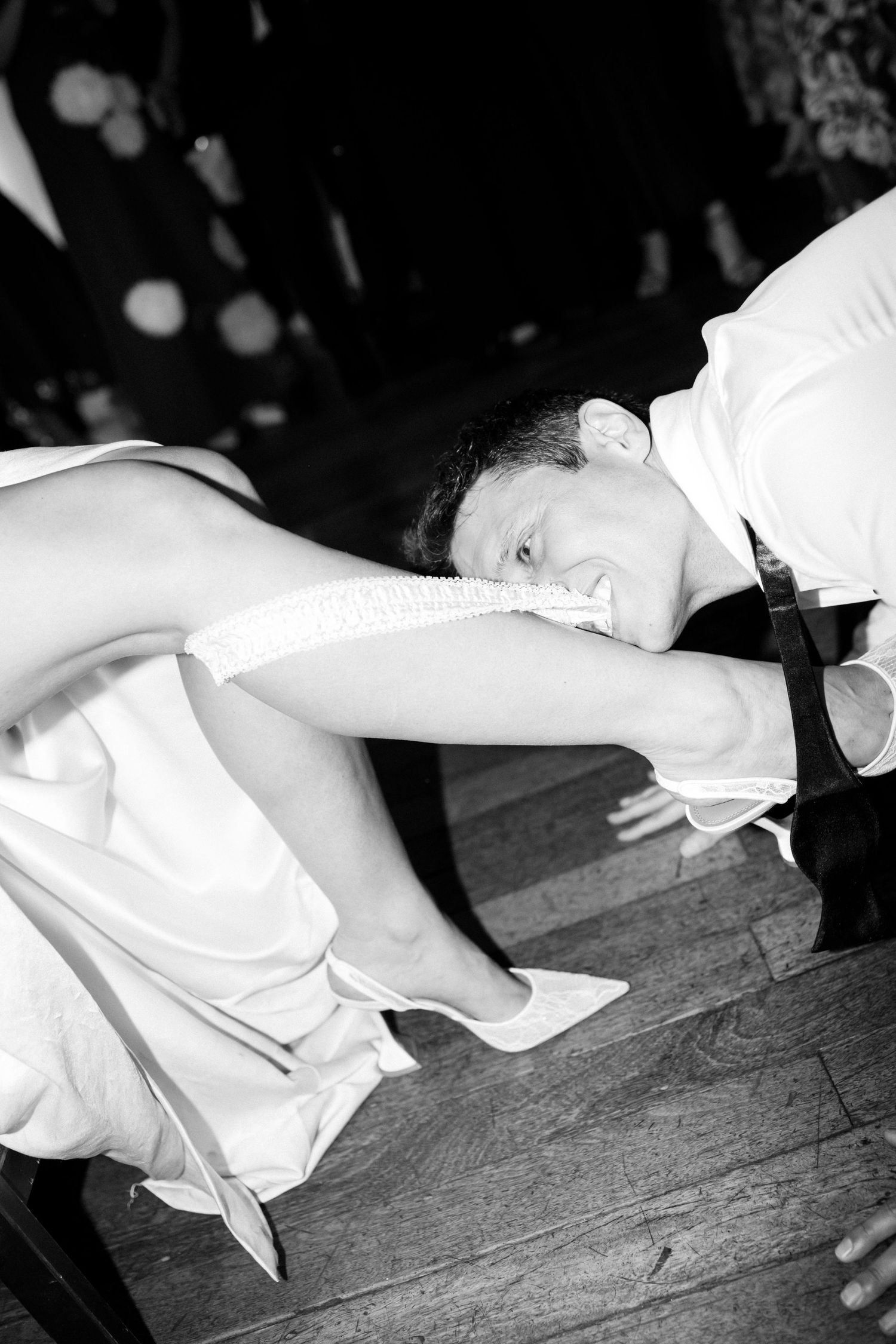 Black and white photo of a groom taking off the bride's garter with his teeth