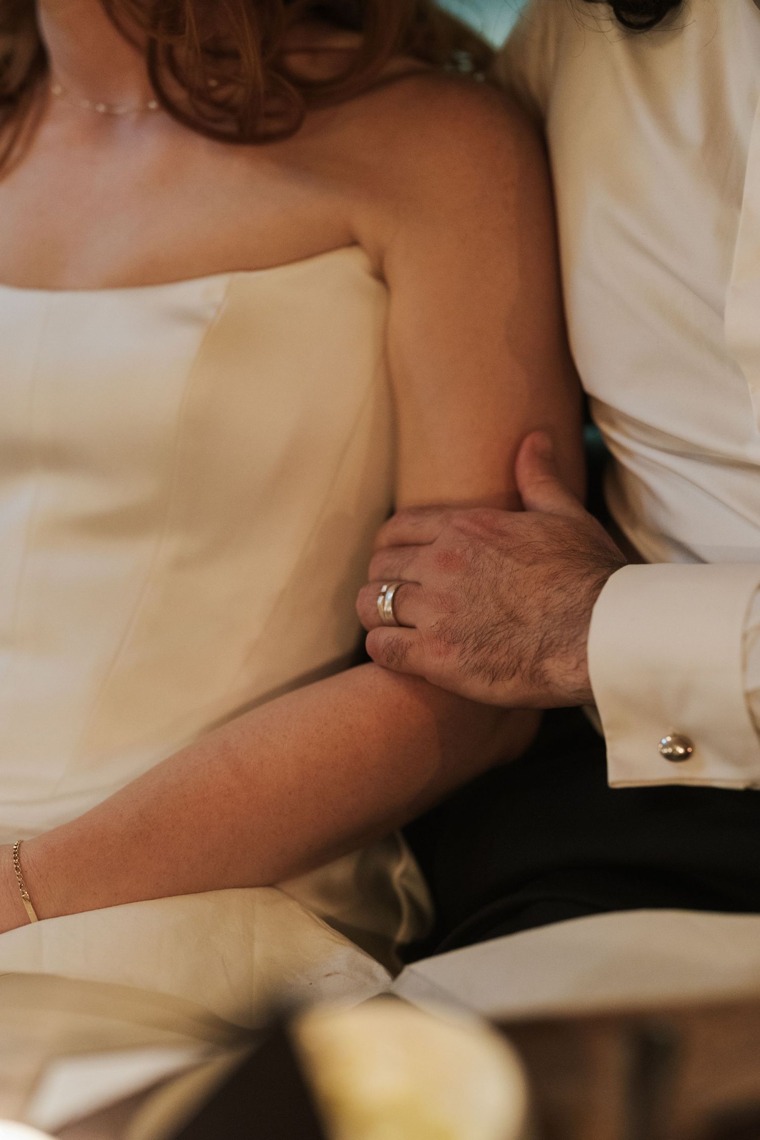 Bride and groom holding hands, showing wedding ring, dressed in white wedding attire during ceremony.