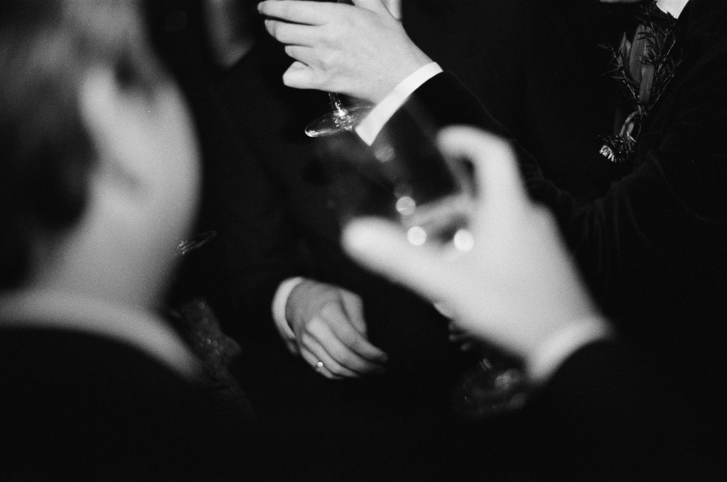 Black and white photo of elegantly dressed guests holding cocktail glasses at a formal wedding reception.