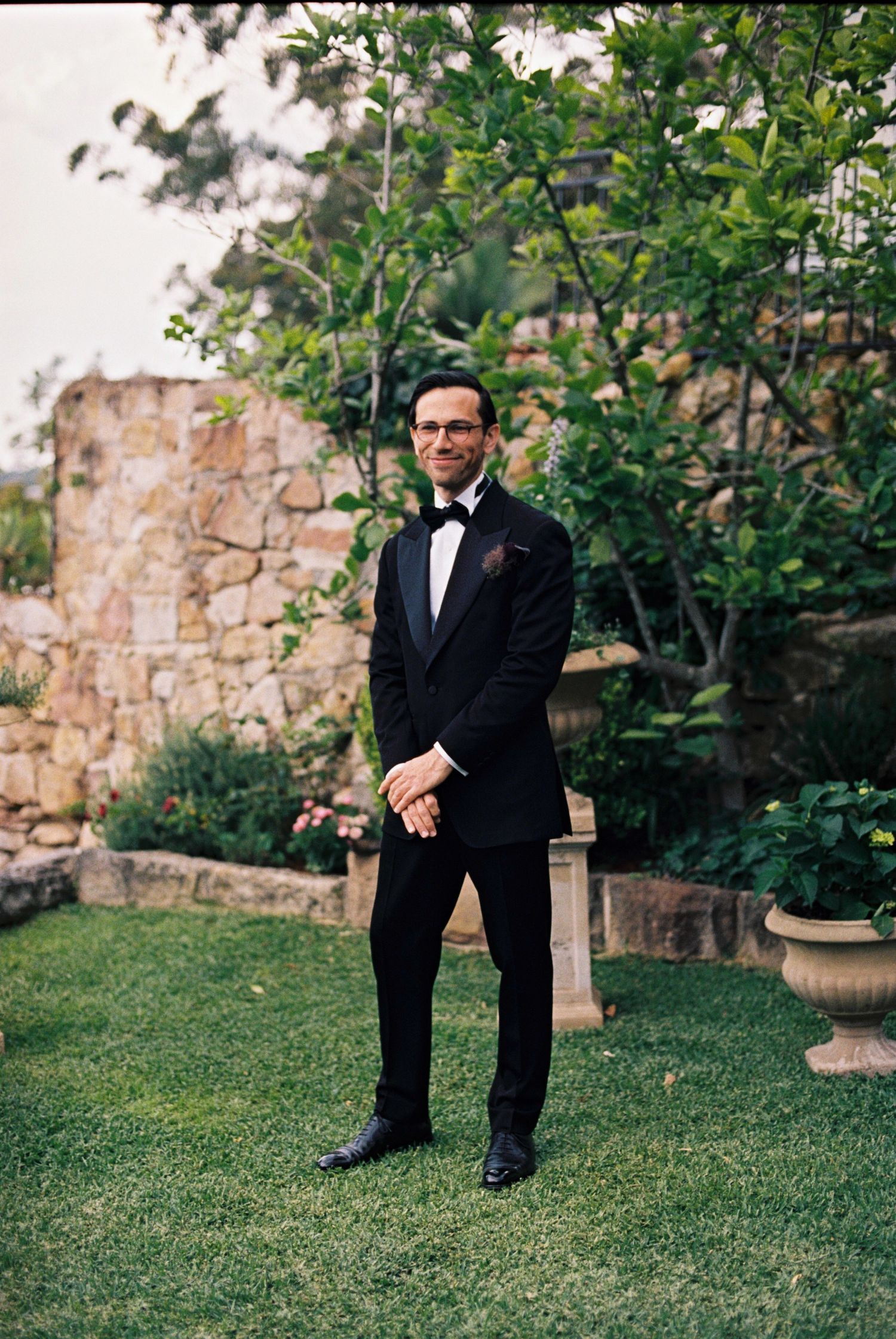 A formal garden setting with stone walls and lush greenery creates an elegant backdrop.