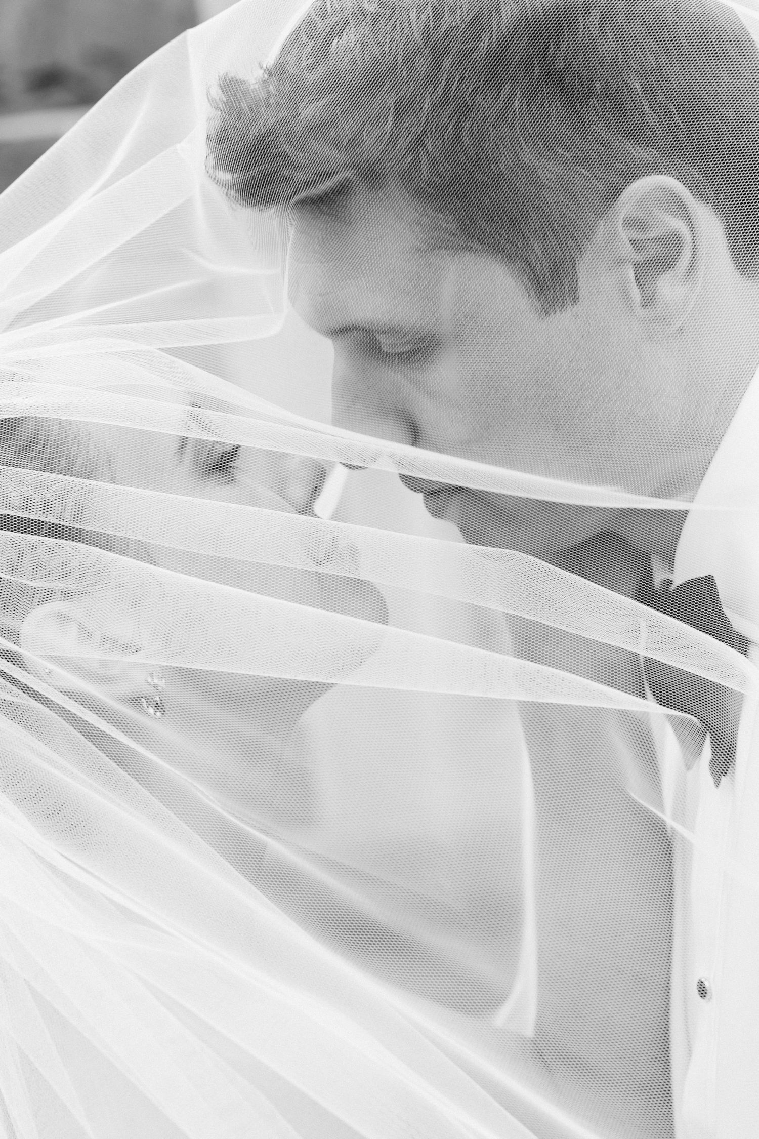 A romantic wedding photo series showing close-up shots of a couple kissing under a flowing white veil.