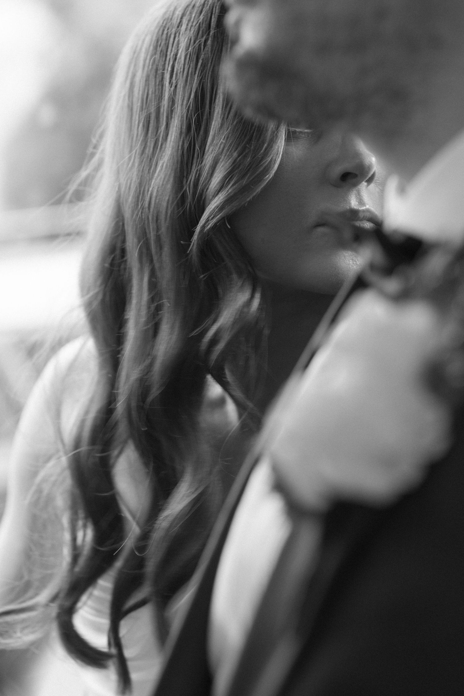 Black and white close-up of a bride with long flowing hair, gazing softly at her groom in an intimate moment.