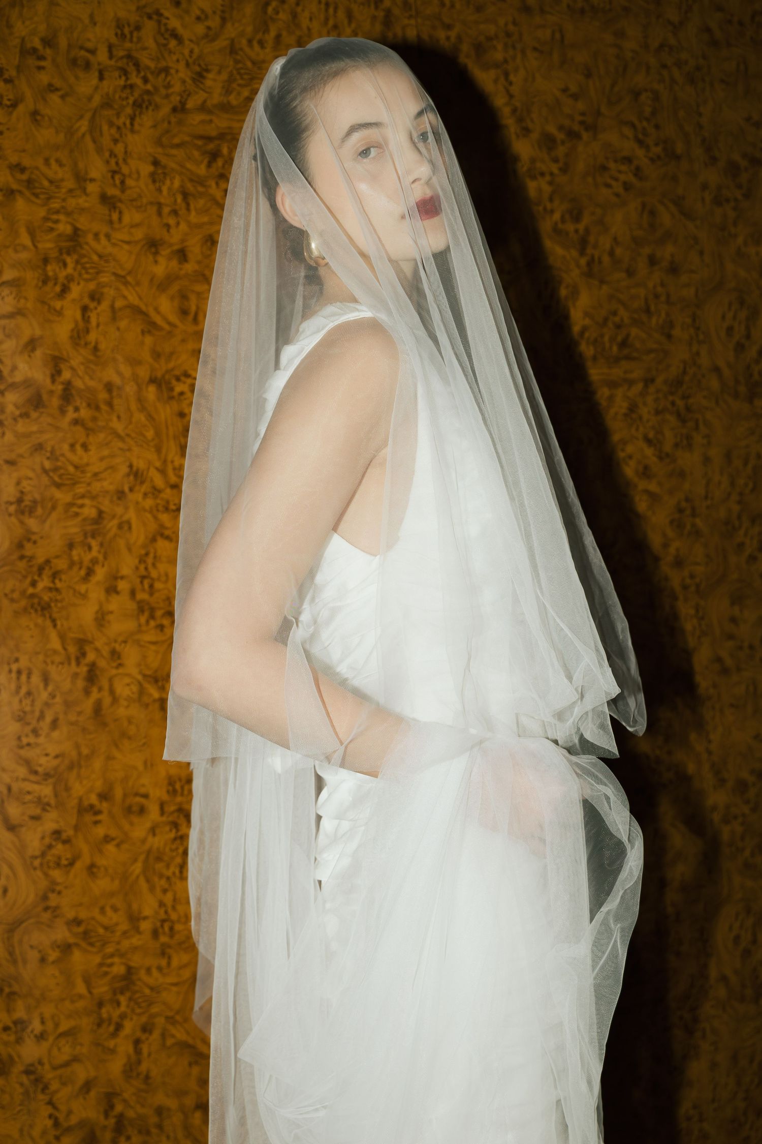 Ethereal bridal portrait with flowing white veil against textured golden wallpaper.