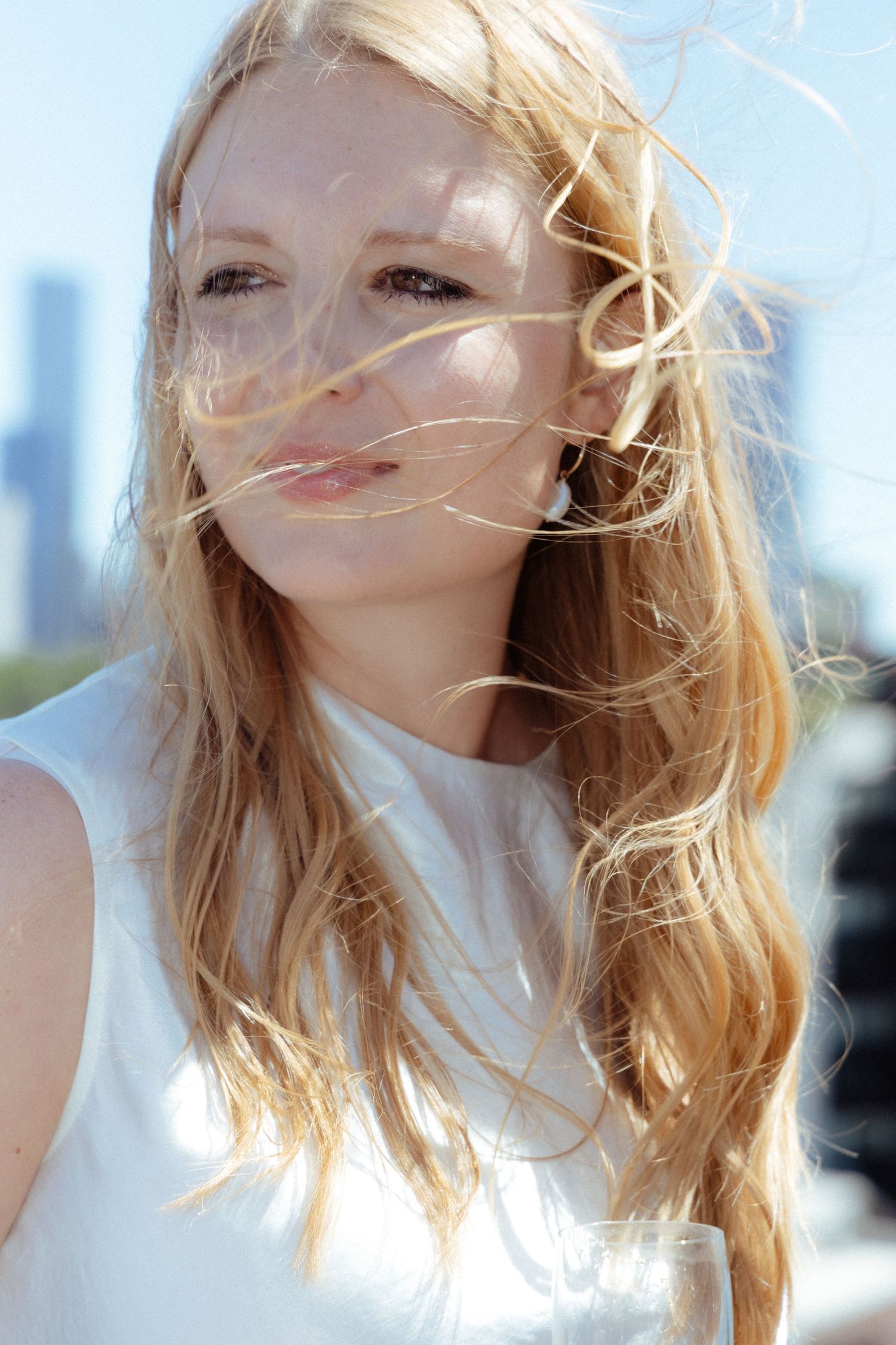 Portrait of a woman with windswept blonde hair against a bright background.