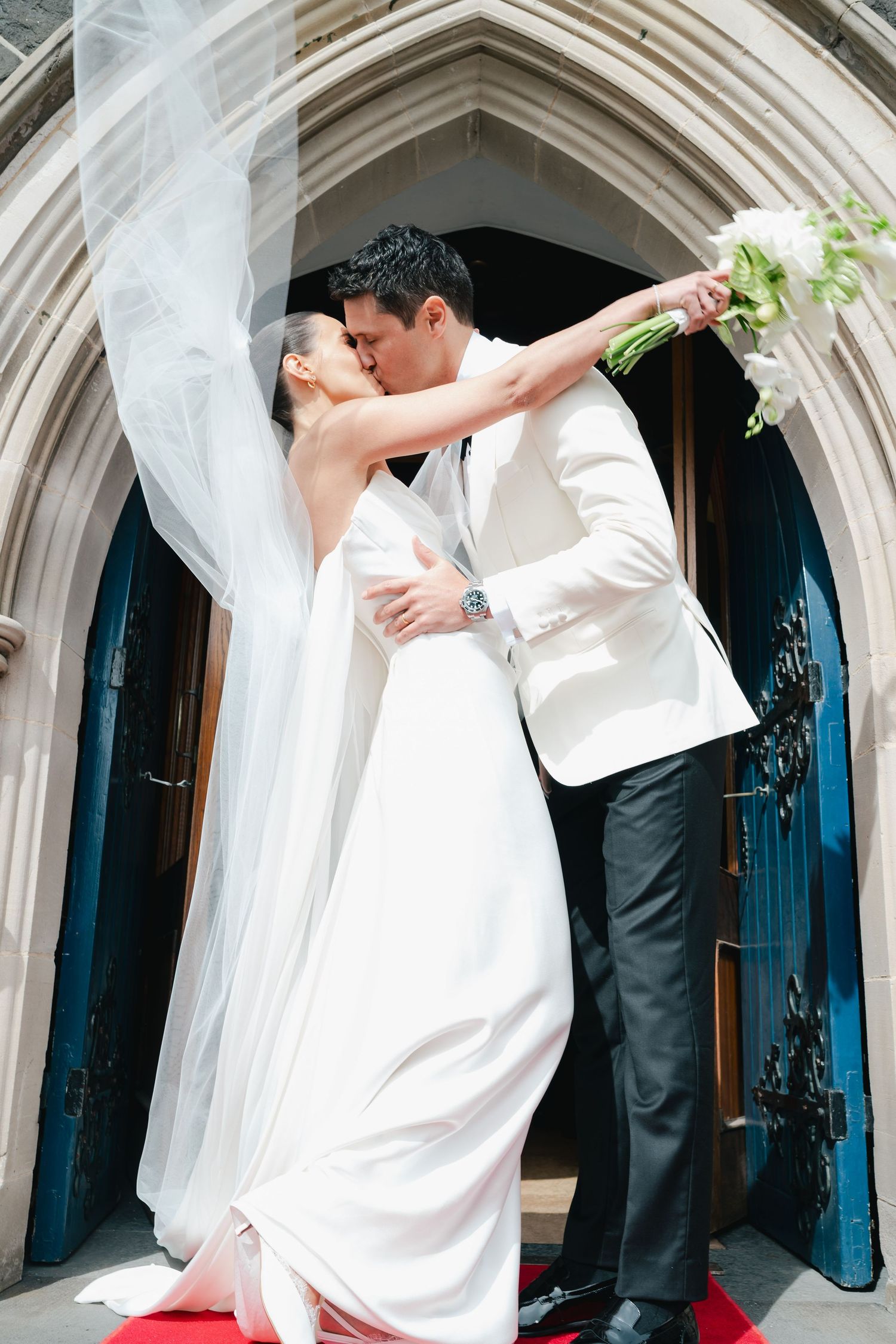 Romantic wedding kiss under gothic stone archway.