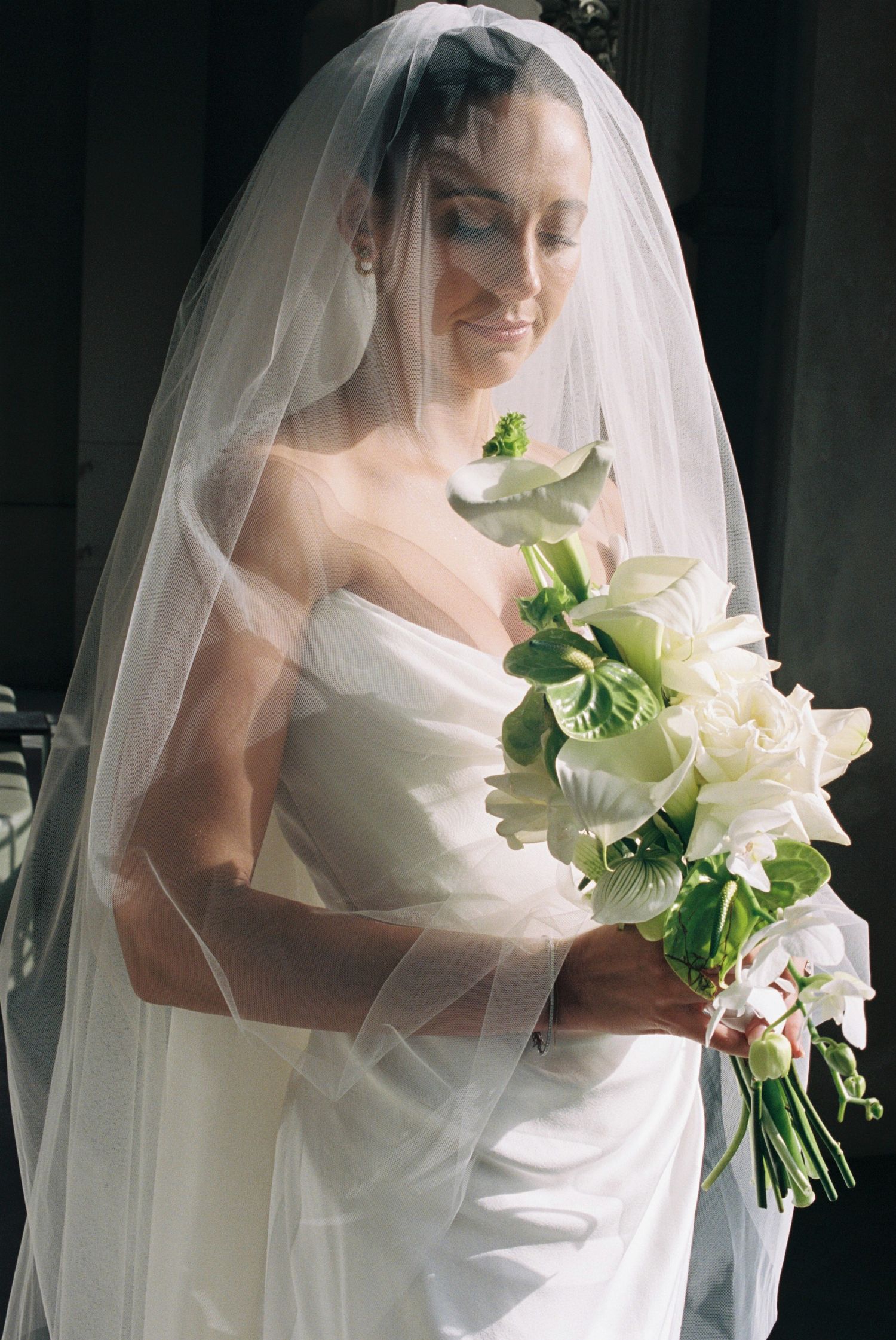 Elegant bride in white gown and veil holding a bouquet of white lilies.