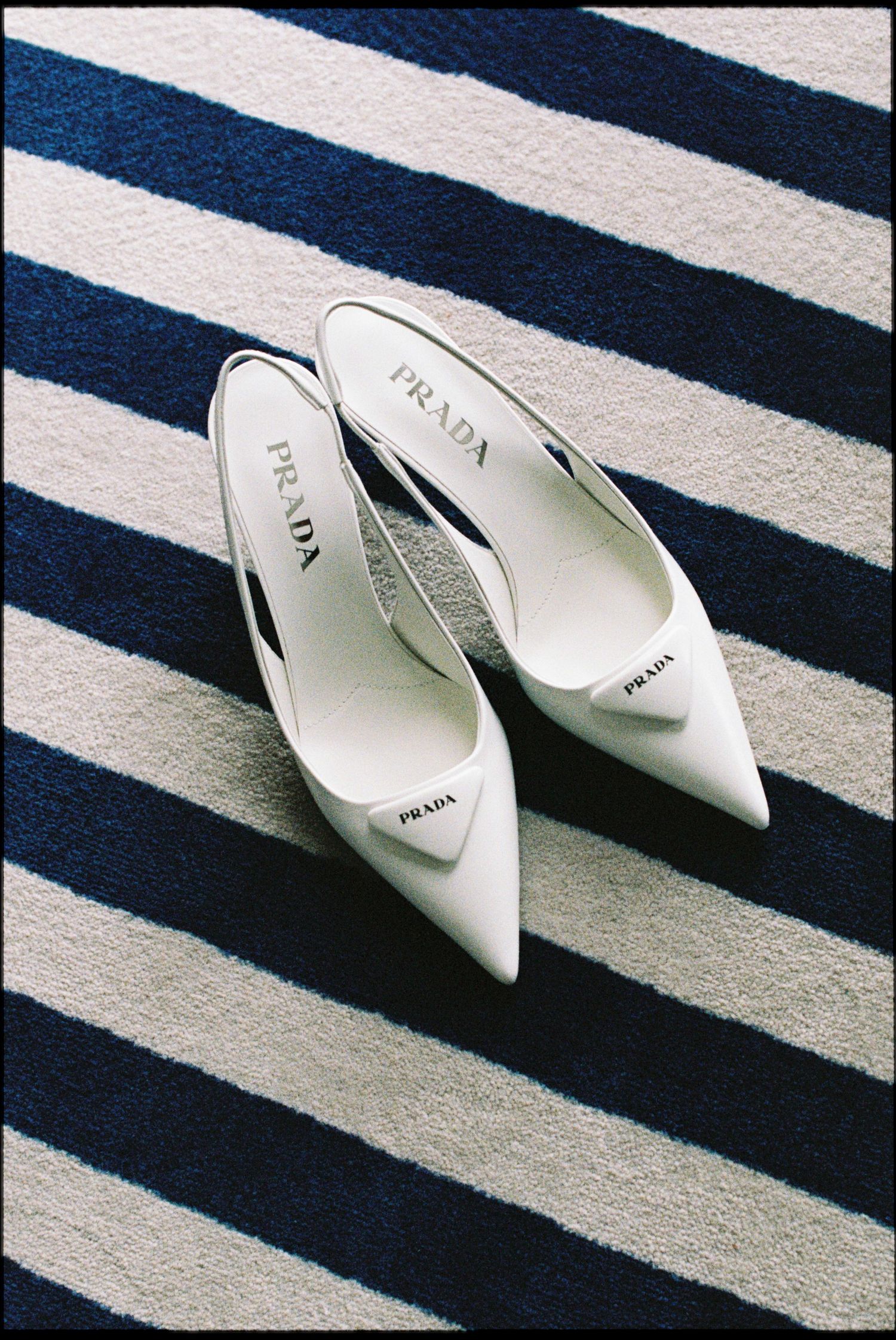 White Prada slingback kitten heels displayed on a navy and white striped surface.