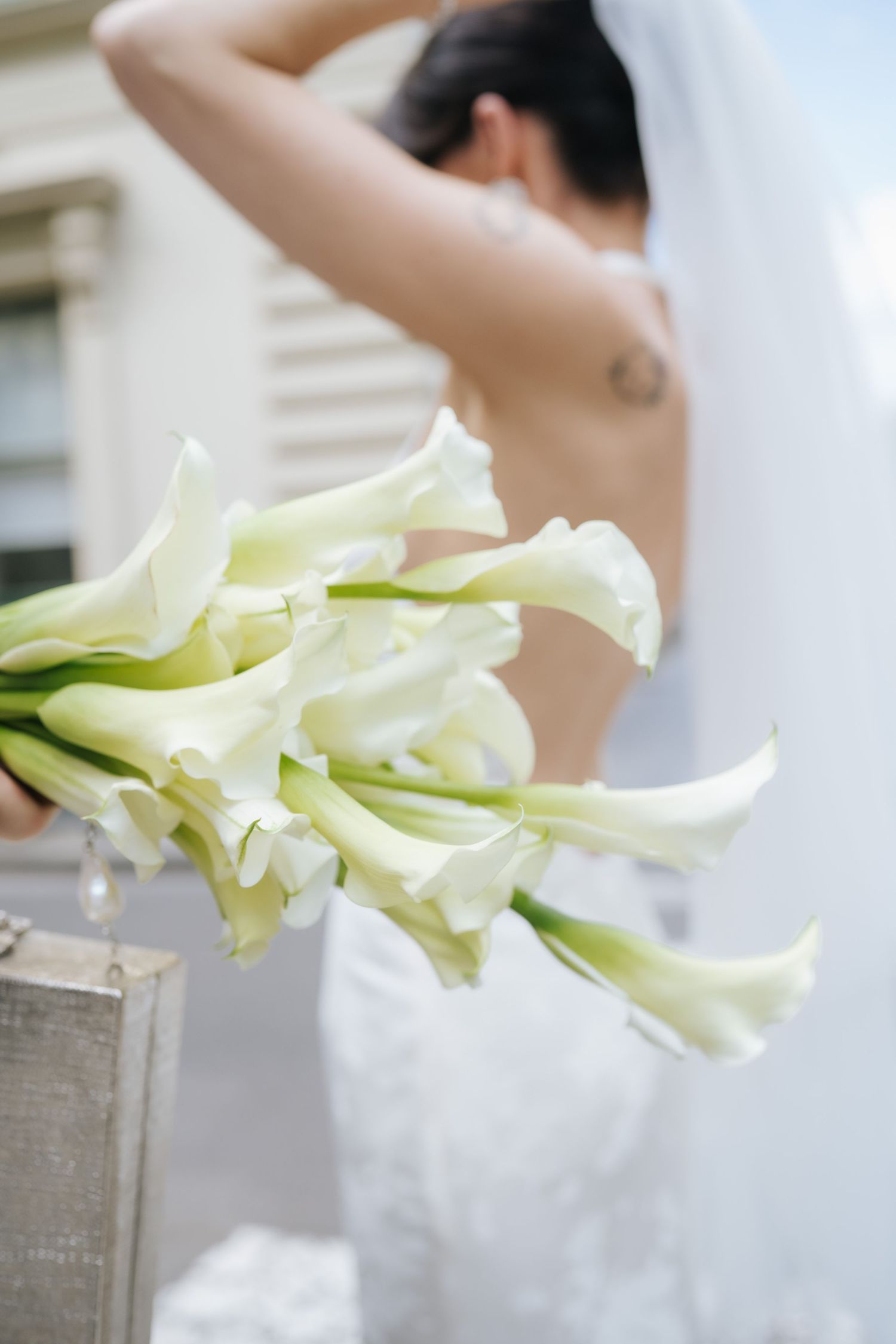 A white calla lily flower arrangement being styled against a light background with elegant minimalist composition.