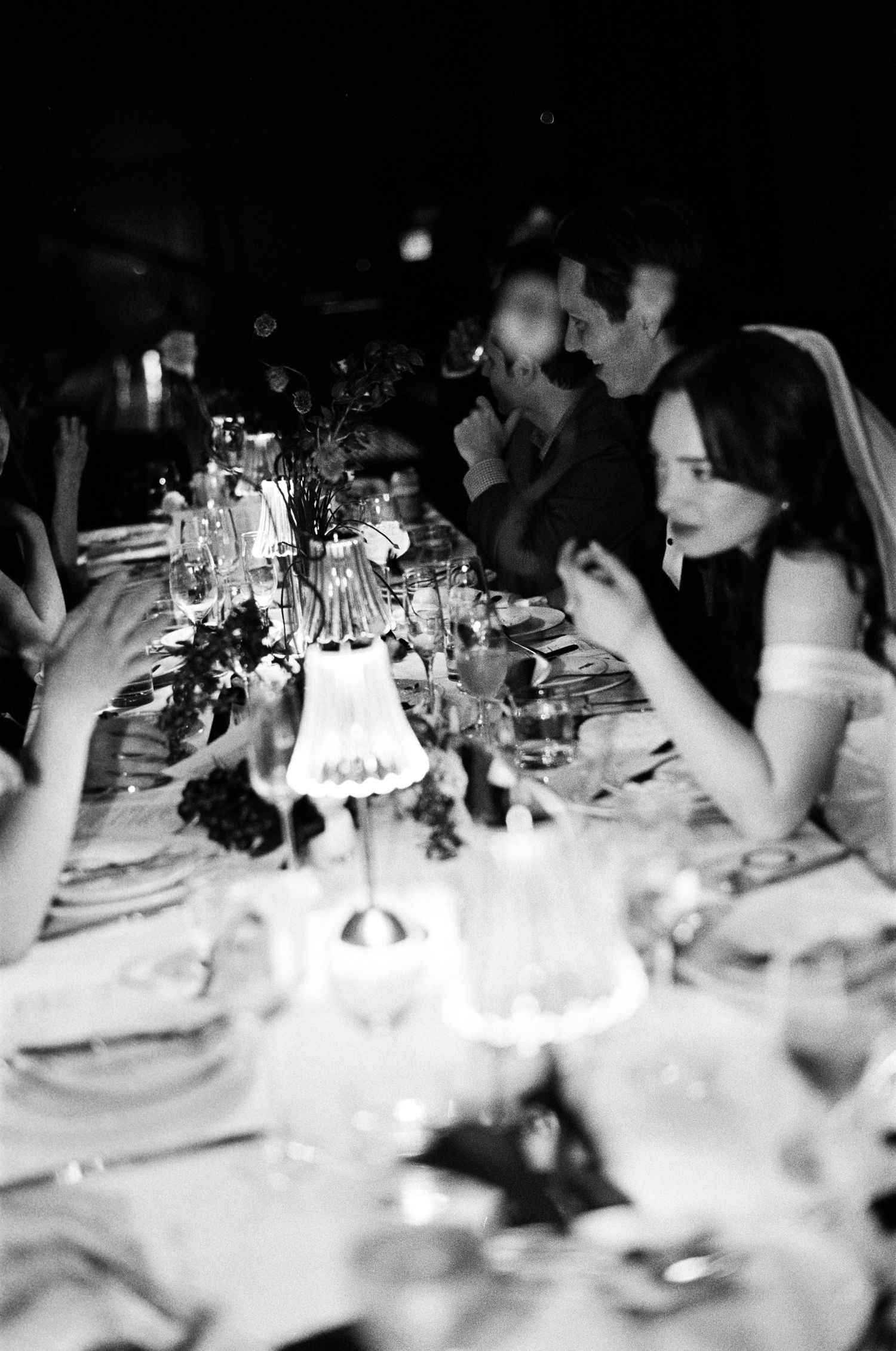 Black and white photo of elegant wedding reception dinner guests seated at a long candlelit table.