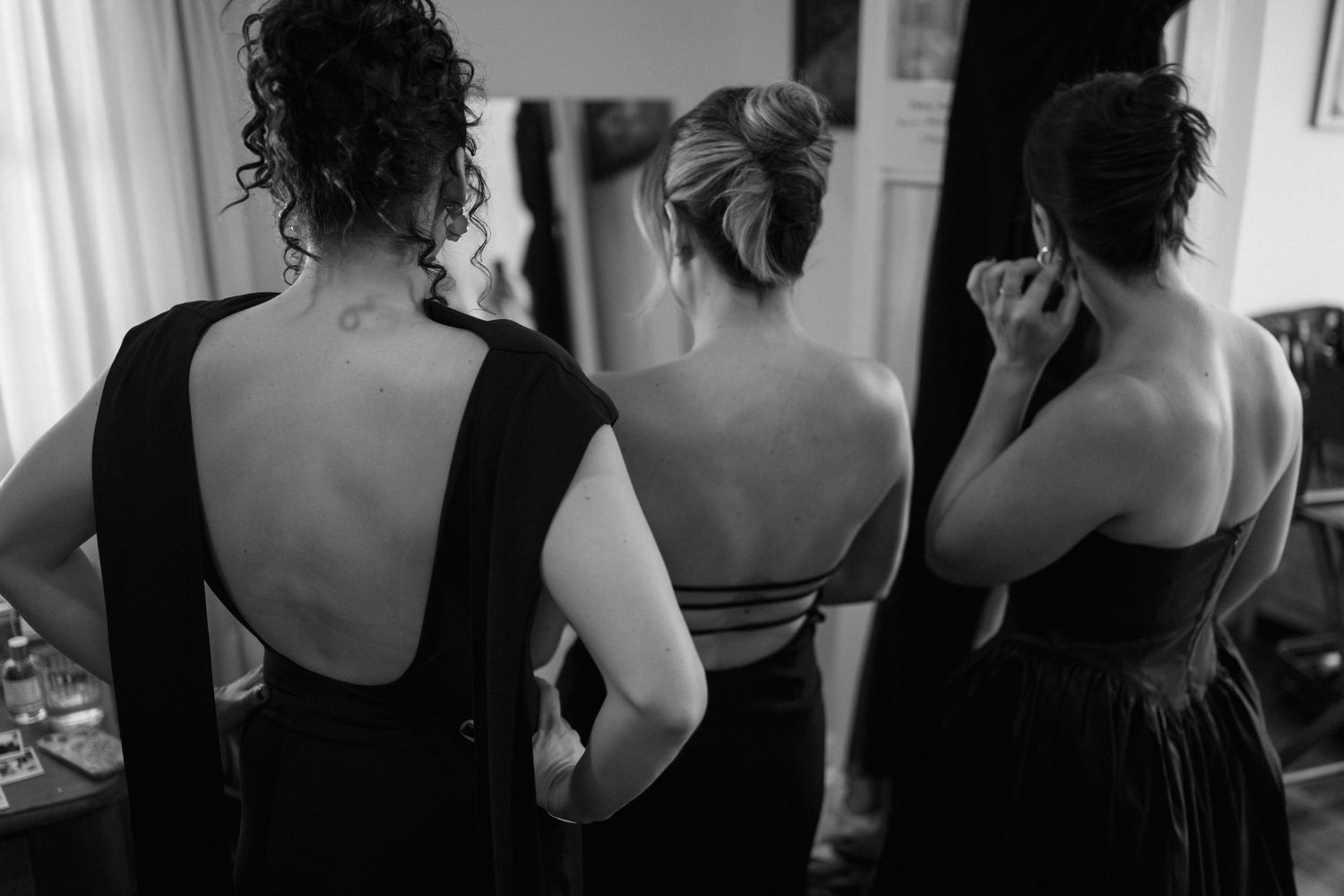 Three bridesmaids in black dresses with open backs stand together before the ceremony.