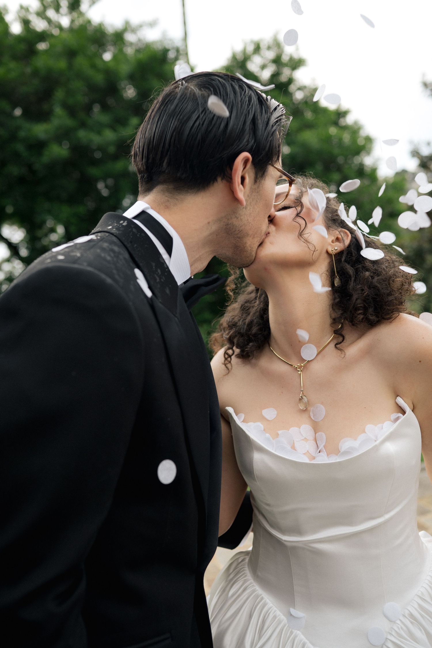 Romantic moment captured with flower petals falling during outdoor wedding celebration.