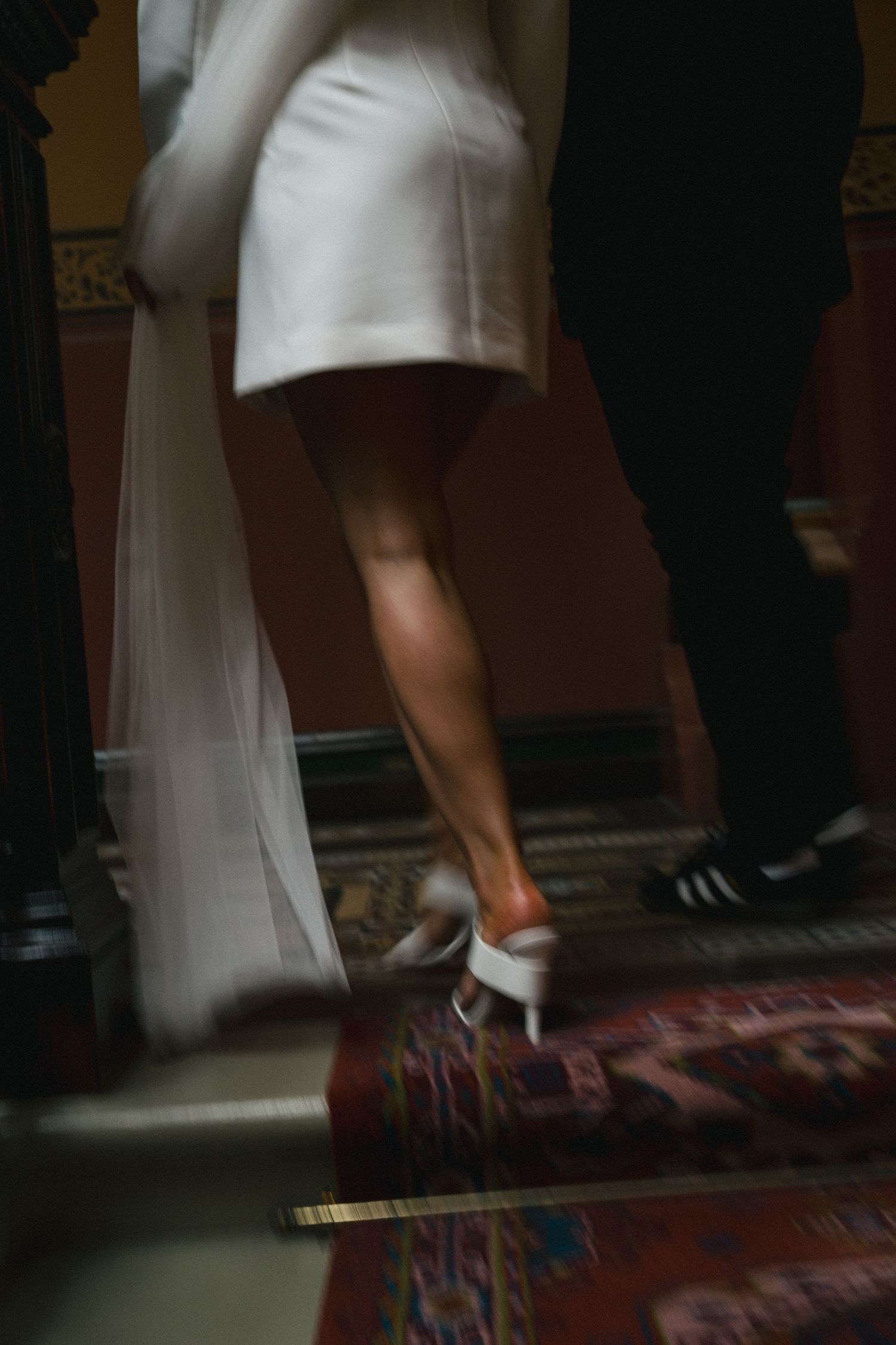 Motion blur of white wedding dress and sneakers dancing on a patterned carpet.