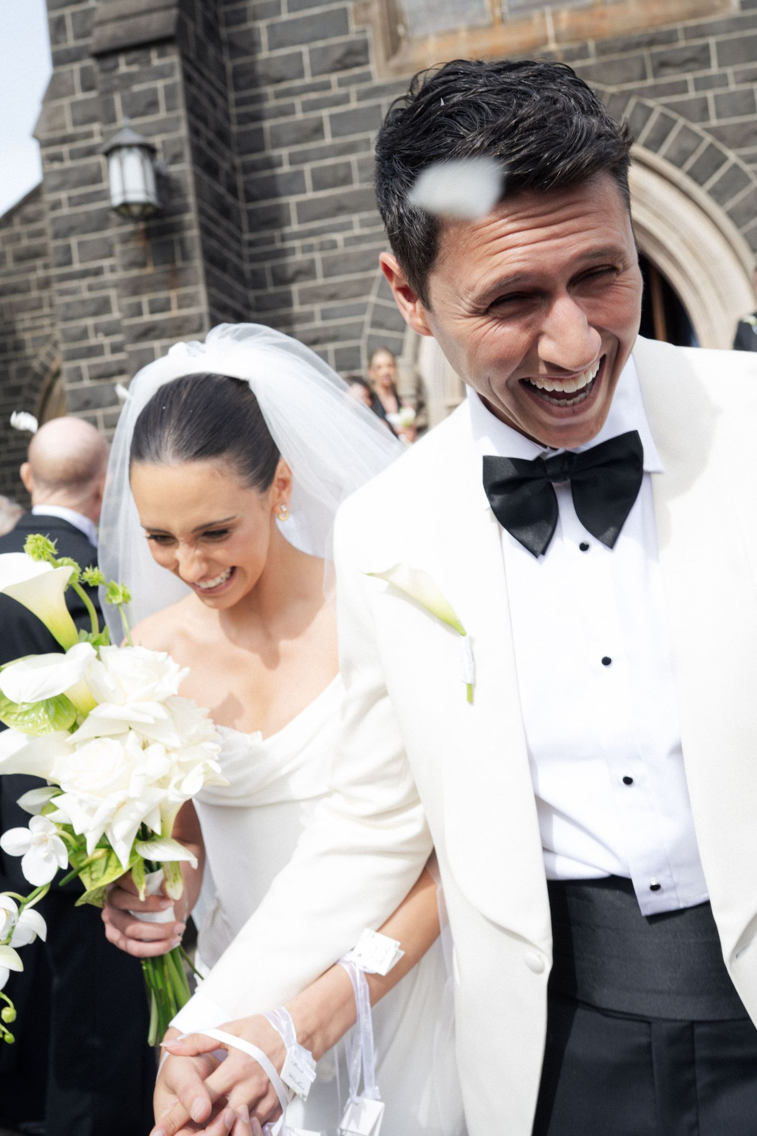 Joyful wedding couple laughing together outside stone church.