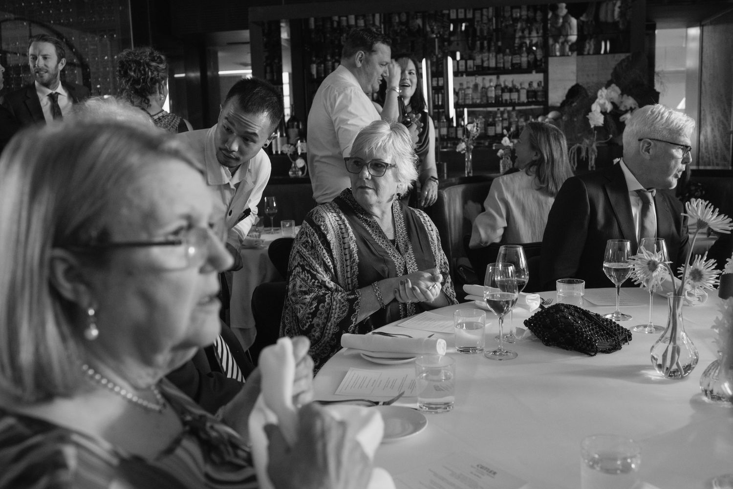 Black and white photo of elegantly dressed seniors dining at a restaurant table during a formal event.