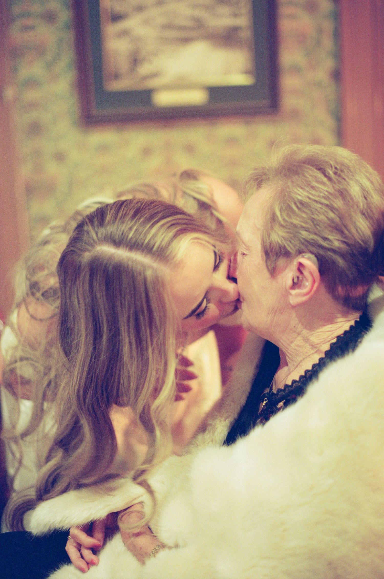 A couple sharing a romantic kiss indoors, with the woman's long blonde hair cascading over her shoulders.