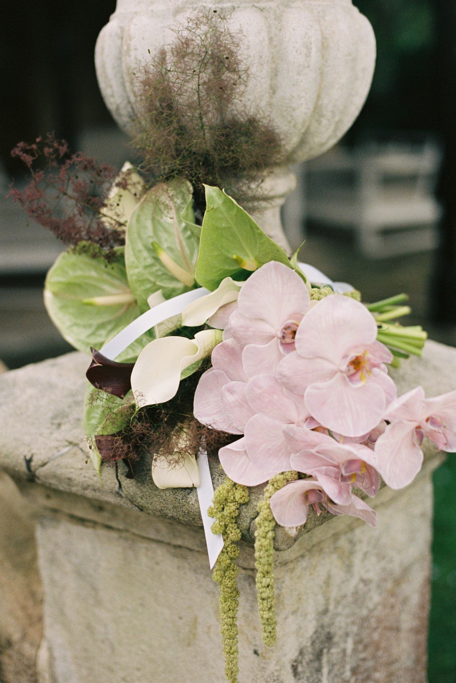 Delicate pink orchids and greenery adorn a weathered stone pillar or column.