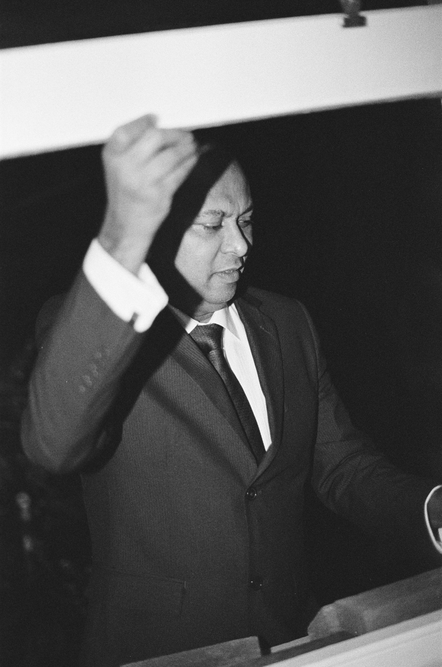 Black and white photo of man in suit raising fist at podium during formal speech or ceremony.