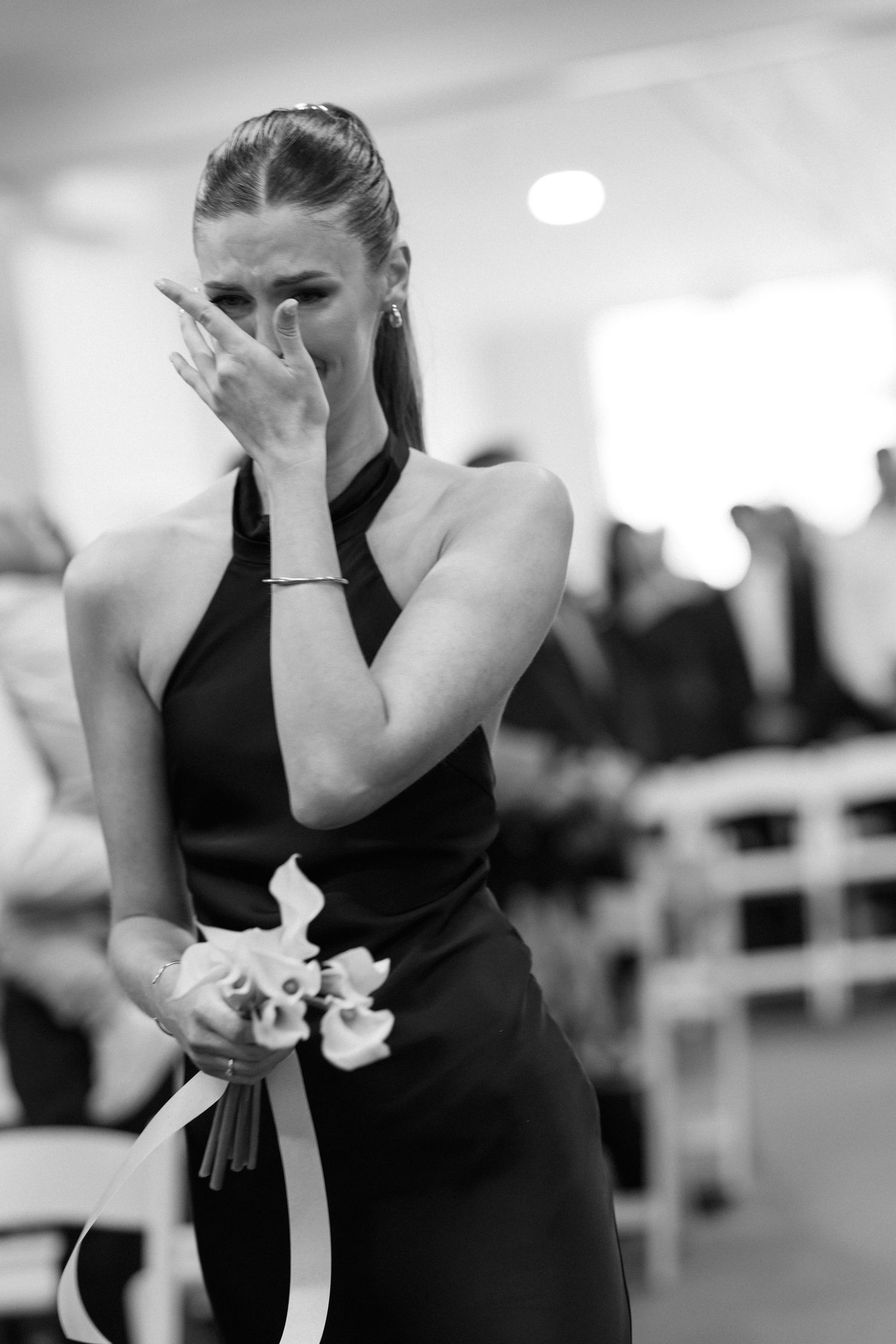 Bridesmaids in black dresses show emotional reactions during a wedding ceremony.