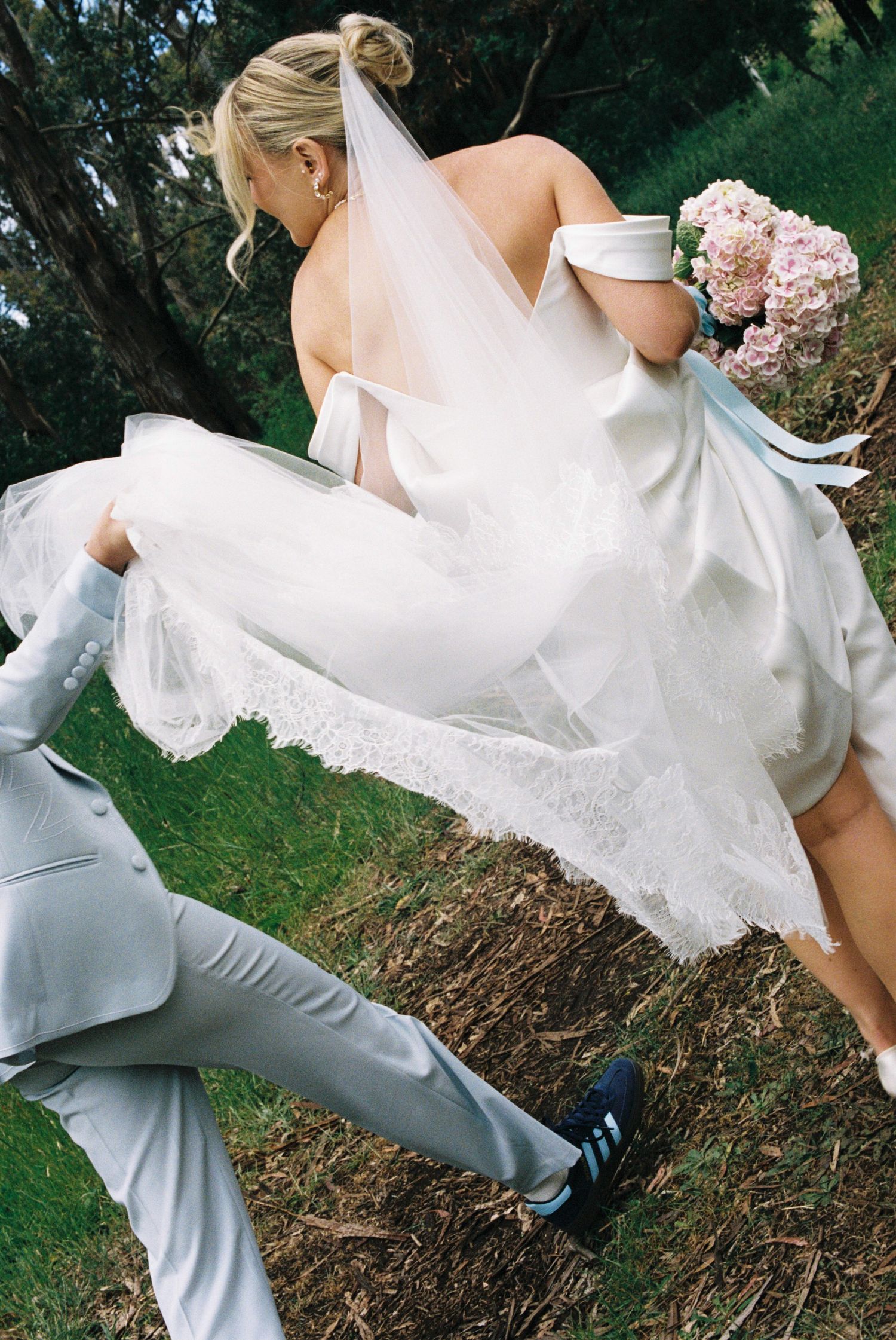 Wedding photography showing movement of white dress and grey pants outdoors.