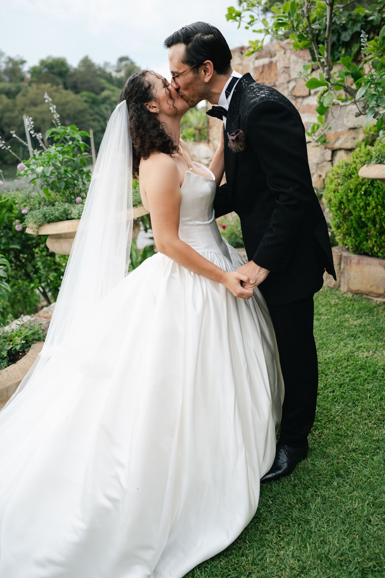 Newlyweds share their first kiss on a garden terrace overlooking scenic views.