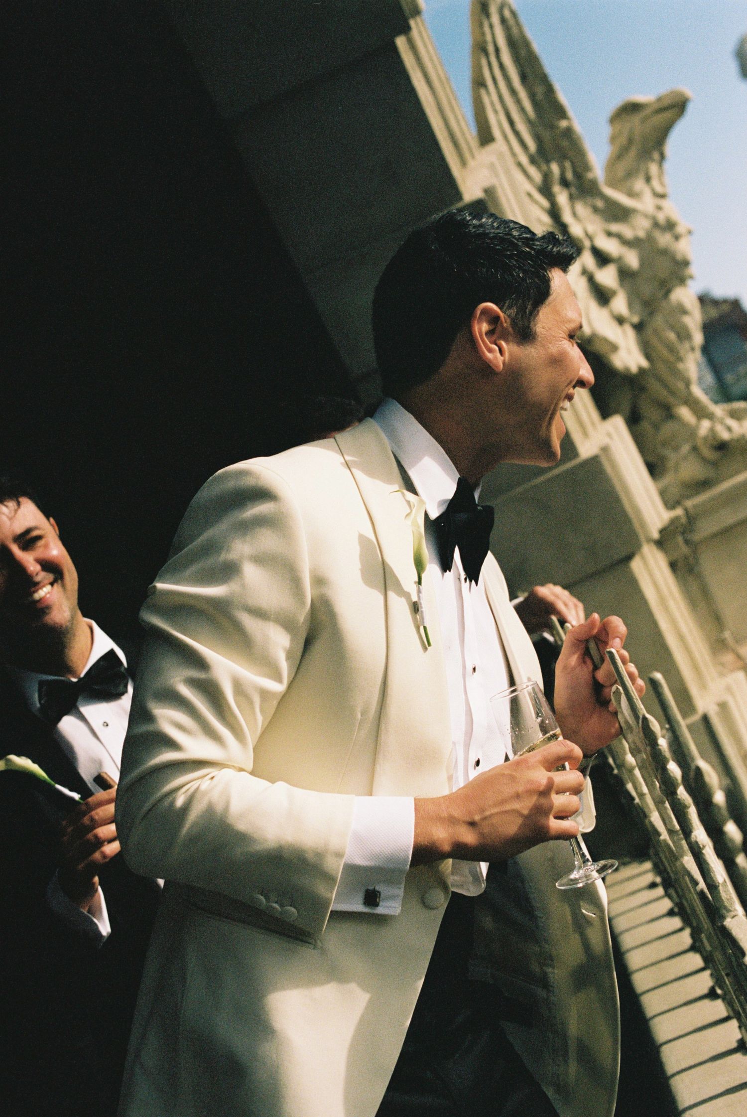 Groom in white tuxedo jacket and bow tie enjoying a celebratory moment.