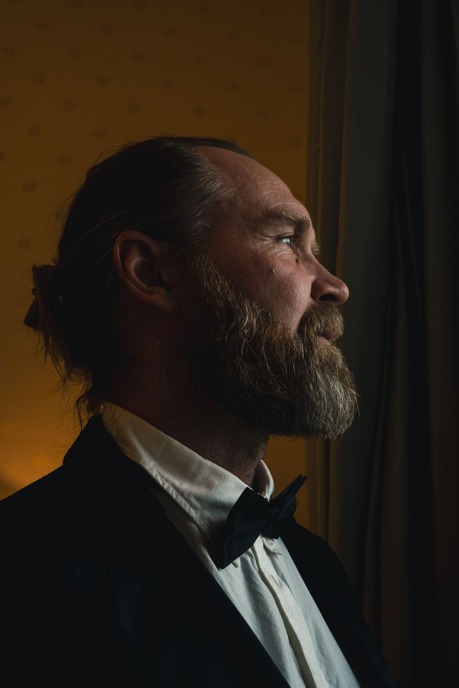 Dramatic side profile portrait in formal attire against warm lighting.