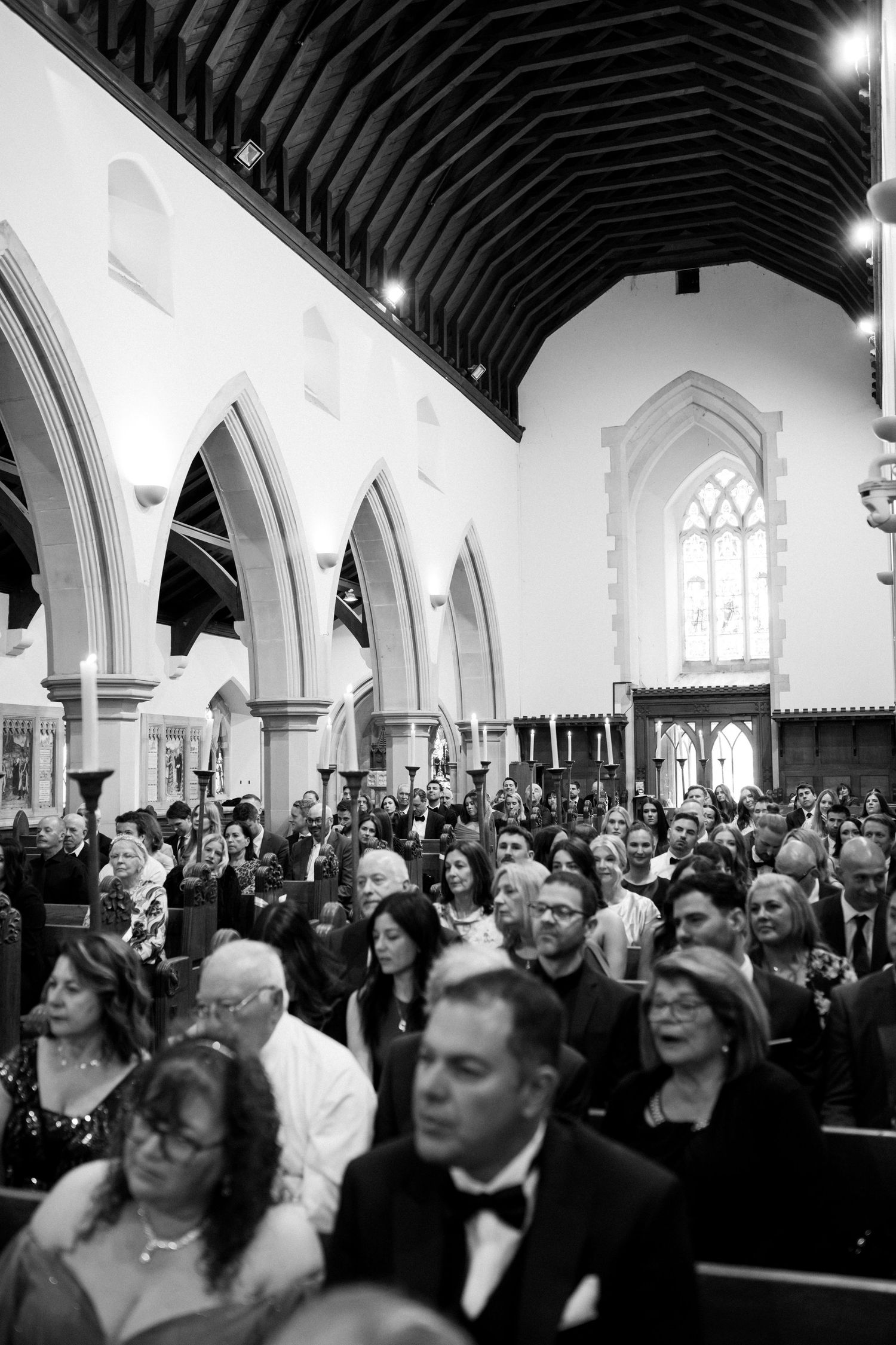 A black and white photo of wedding guests gathered inside a traditional church with vaulted ceilings.