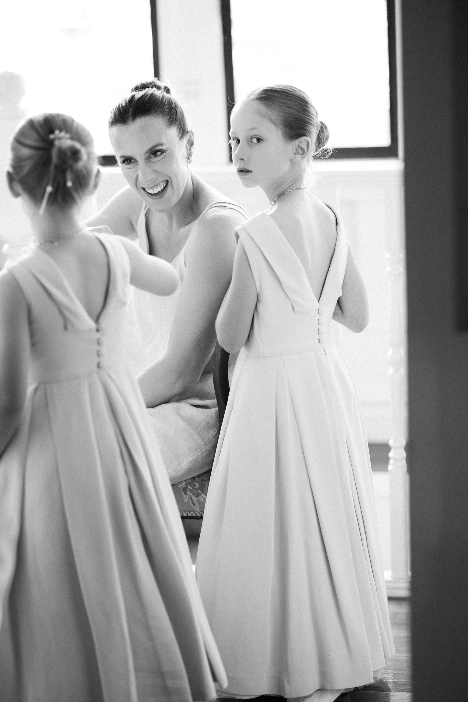 Bridesmaids in elegant white dresses share a candid moment during wedding preparations.