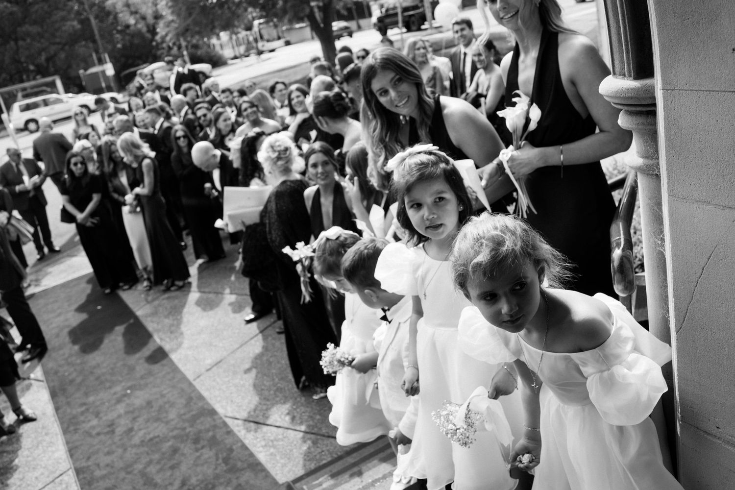 Children in white dresses dance and twirl together at a festive celebration in a crowded venue.