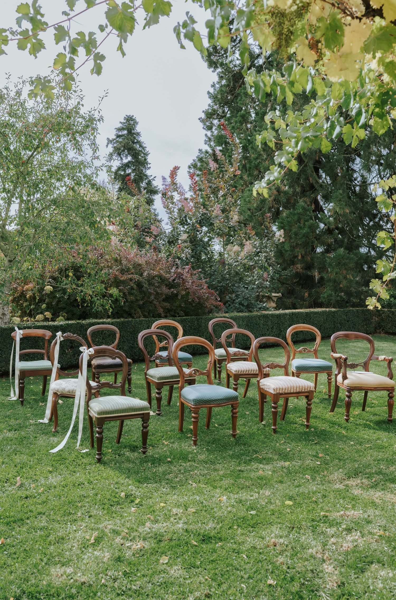 Vintage wooden balloon-back chairs arranged on green lawn for an outdoor garden wedding ceremony.