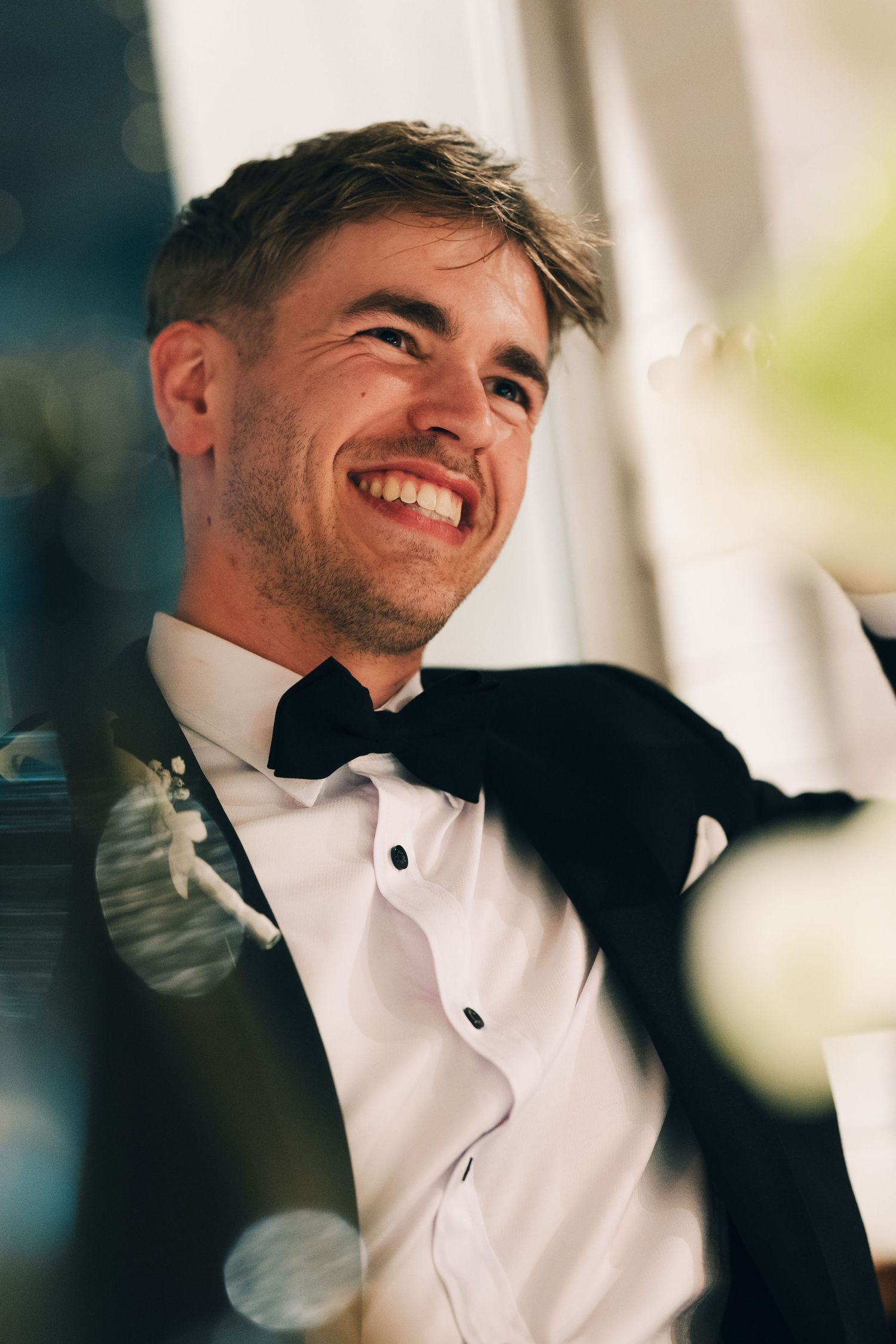 A groom in a tuxedo laughs joyfully during wedding celebrations.