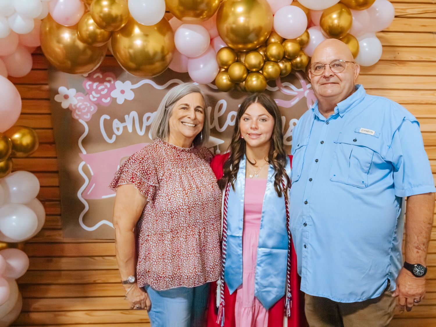 Family celebrating graduation with balloons and congratulations sign backdrop.