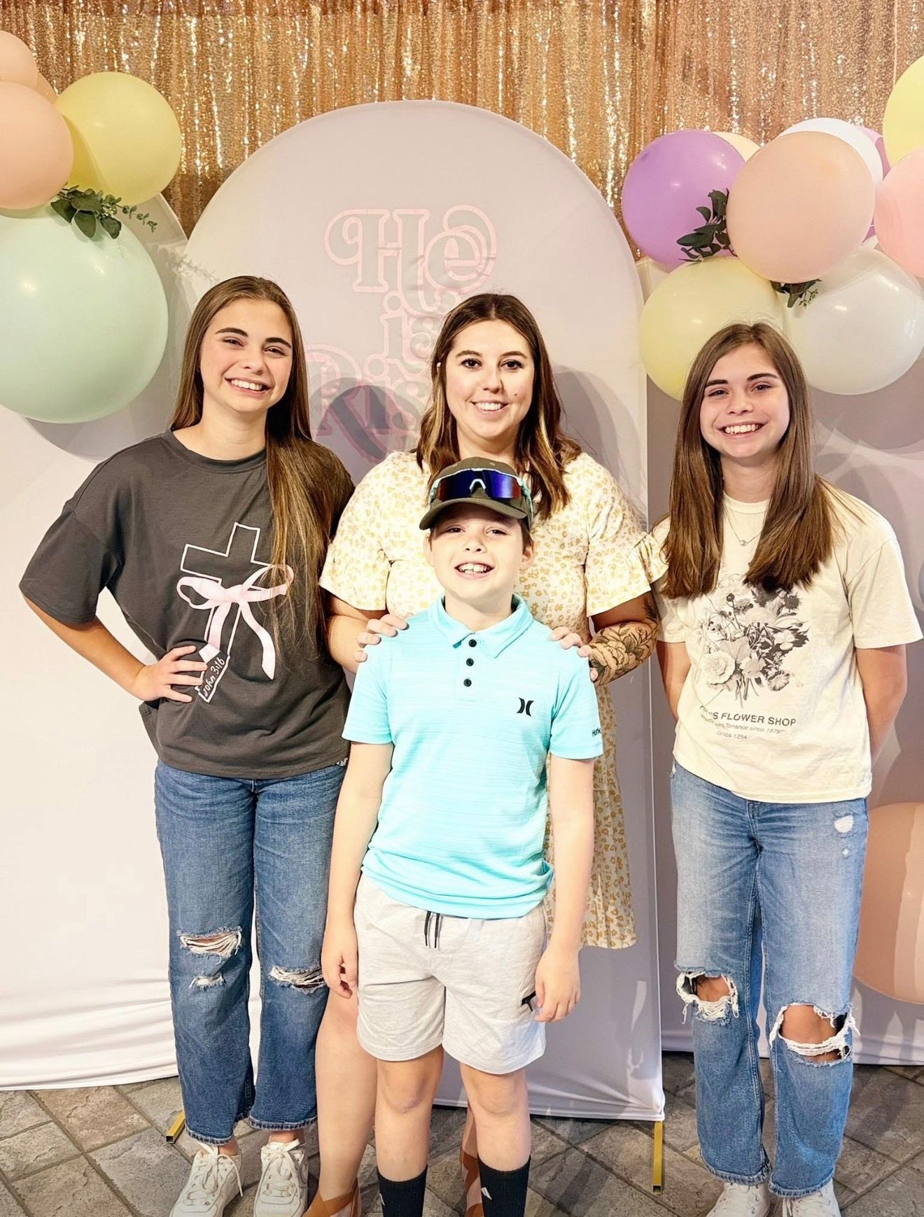 Group photo against a gold sequin backdrop with pastel balloons and decorations.