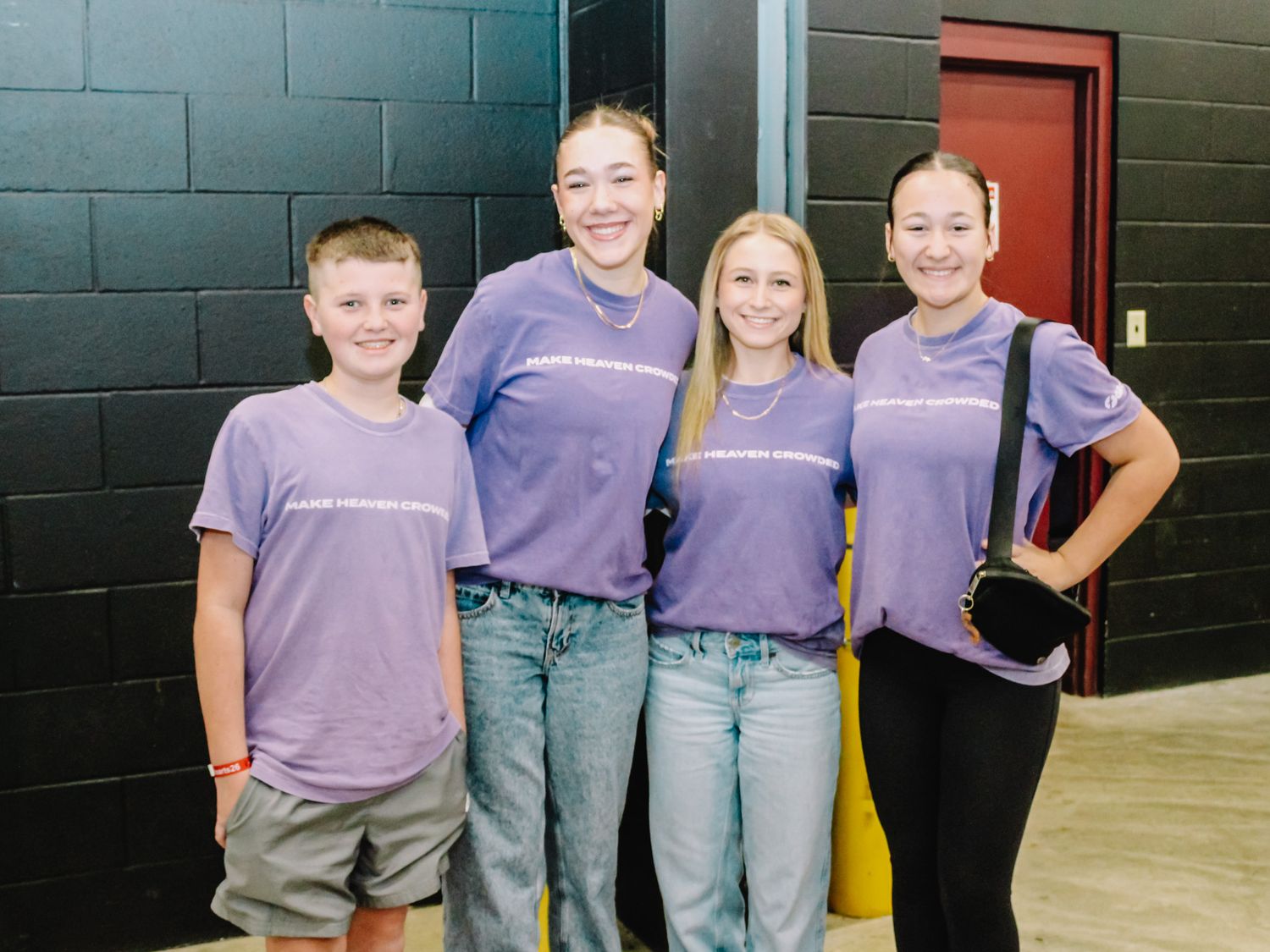 Four young people wearing matching purple t-shirts smiling together at an indoor event venue.