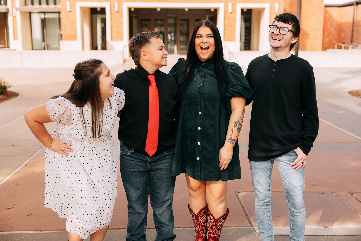 Four people smiling and laughing together outdoors in front of a brick building, dressed in semi-formal attire.