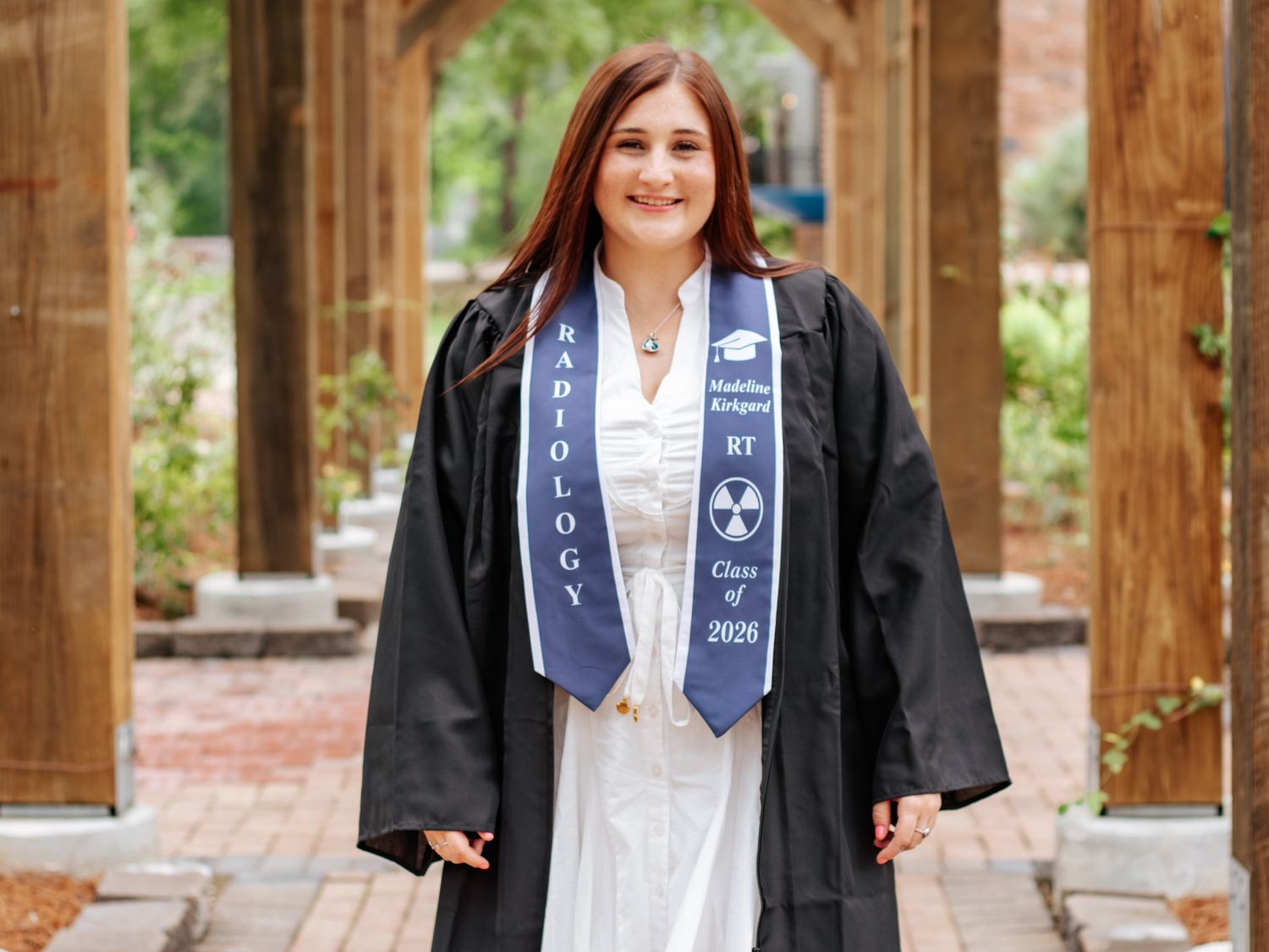 Radiology graduate in black gown and blue stole smiles outdoors, celebrating Class of 2026 graduation.