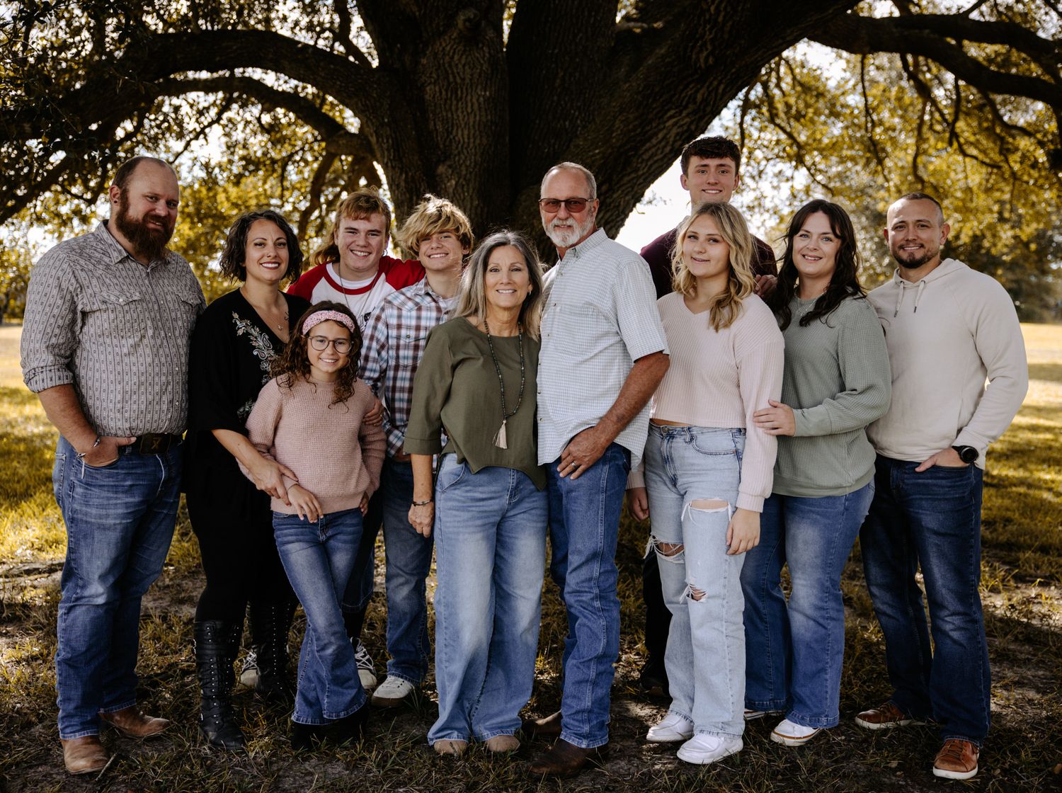 A casual outdoor family photo session showing a group in coordinated blue jeans and neutral tops.
