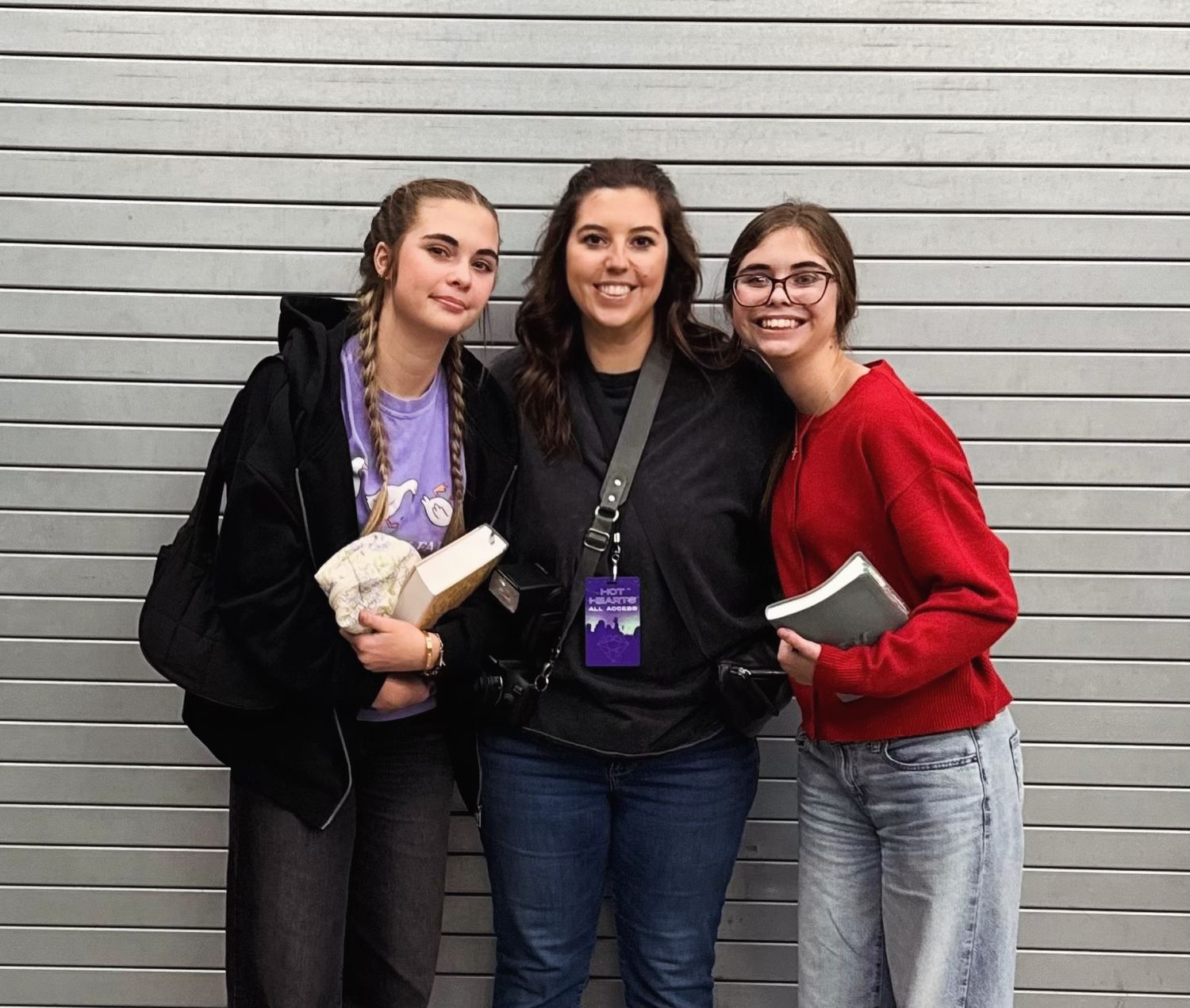Three students wearing casual winter attire pose together against a gray wall while holding books.