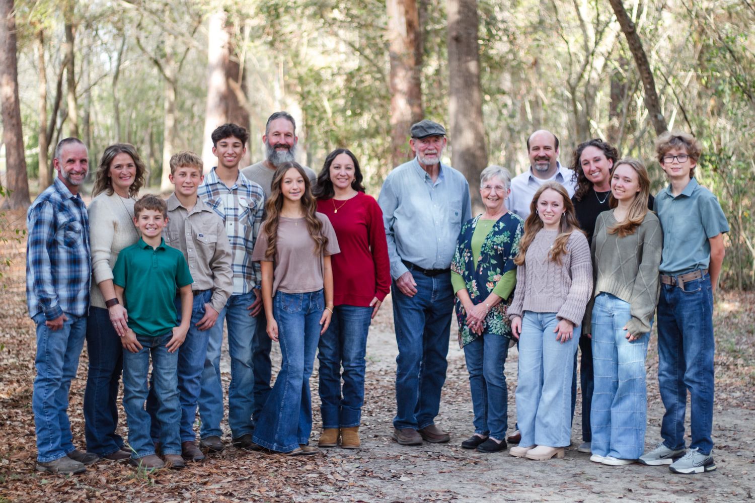 Large multigenerational family group portrait outdoors in a wooded setting, smiling together for a formal photo.