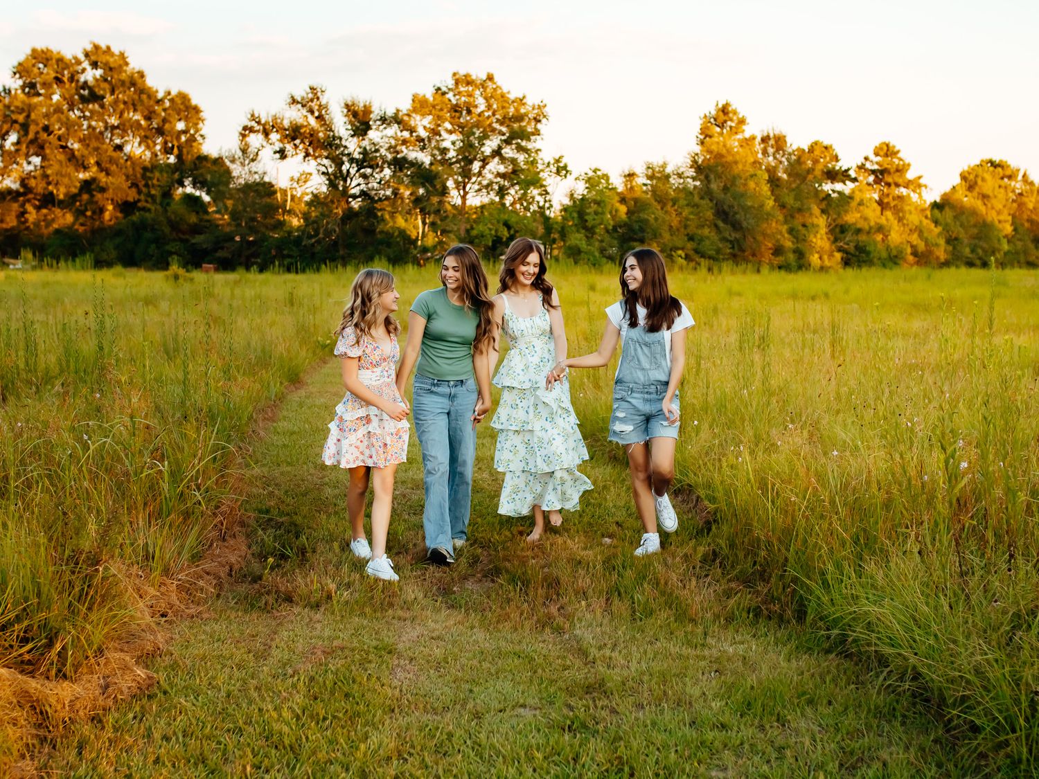 Four girls walking together through a lush green field at golden hour sunset.