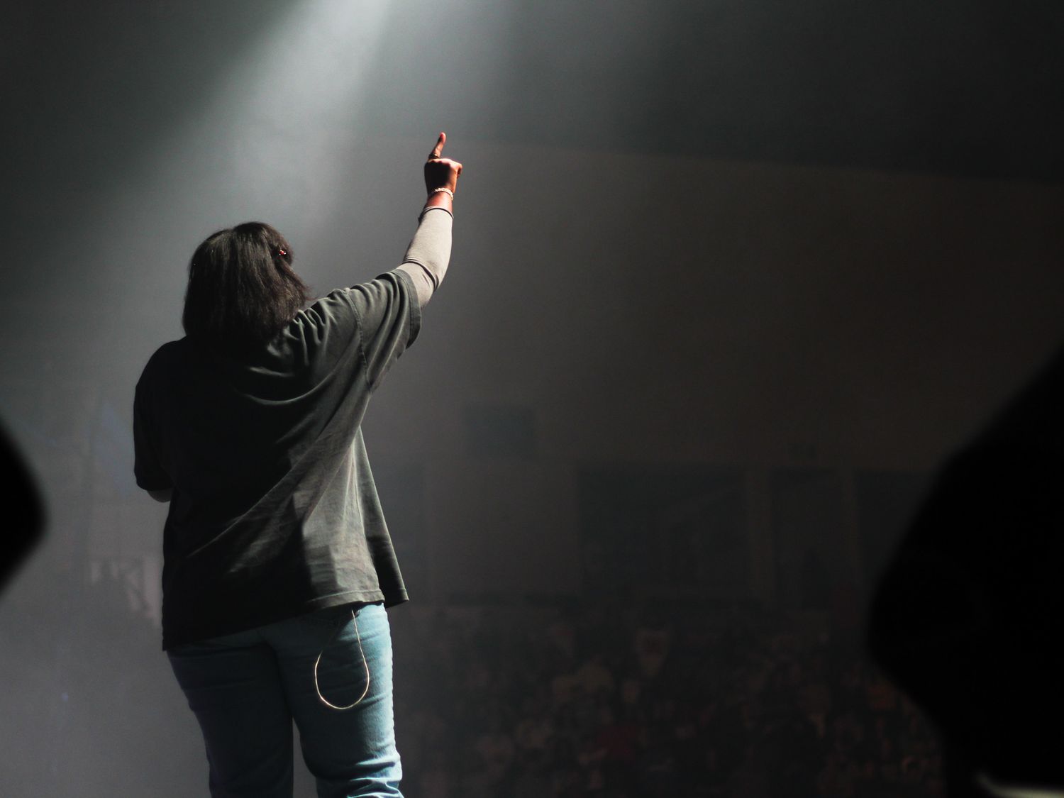 Performer on stage raising one finger to crowd in darkened concert venue.