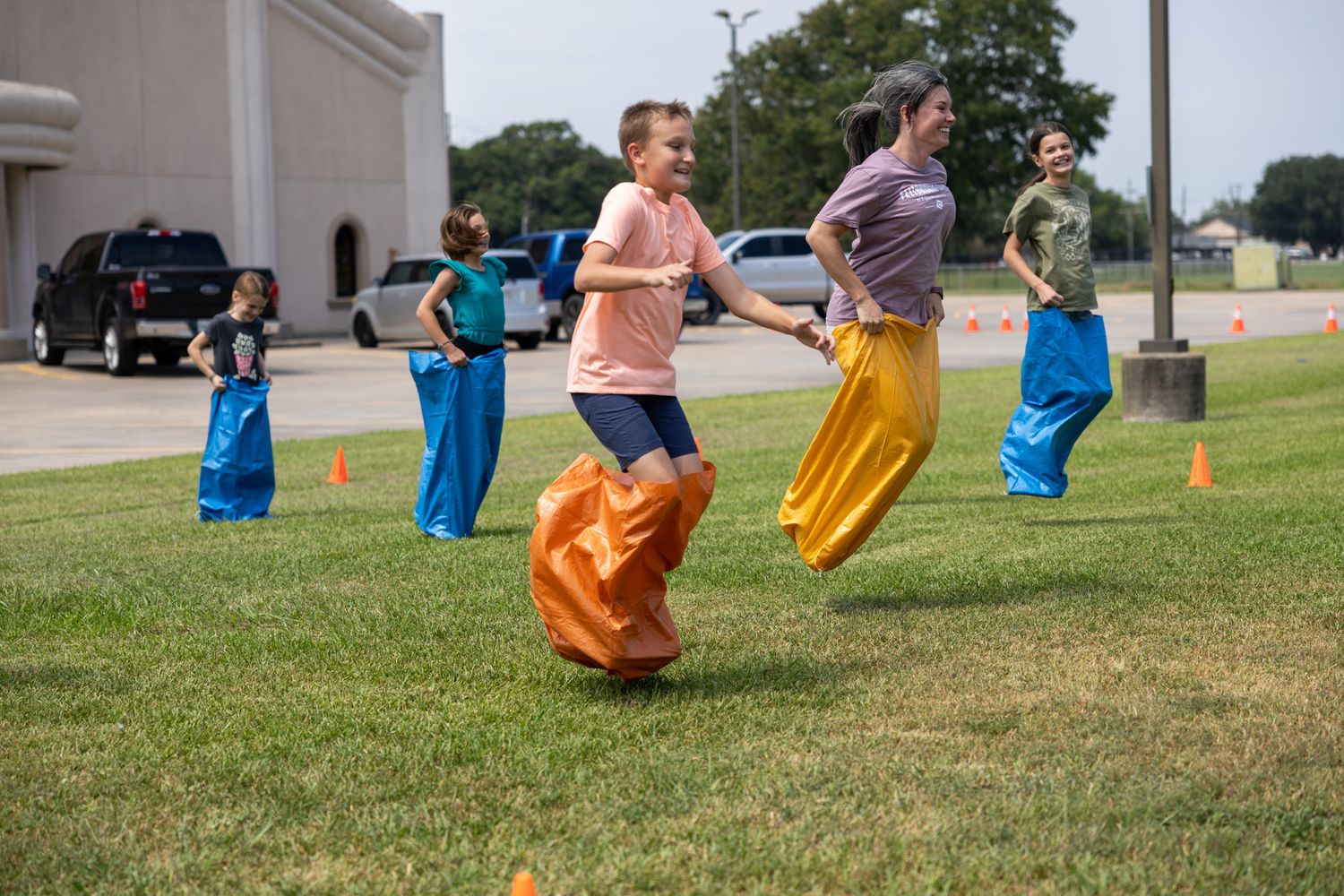 Children competing in a colorful sack race on green grass during an outdoor summer event.