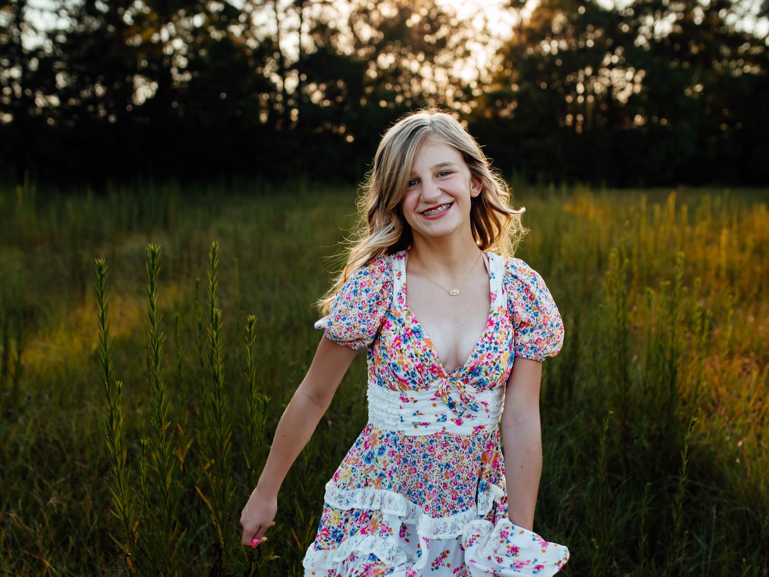 Smiling young woman in floral dress twirling in a sunlit green meadow at golden hour.