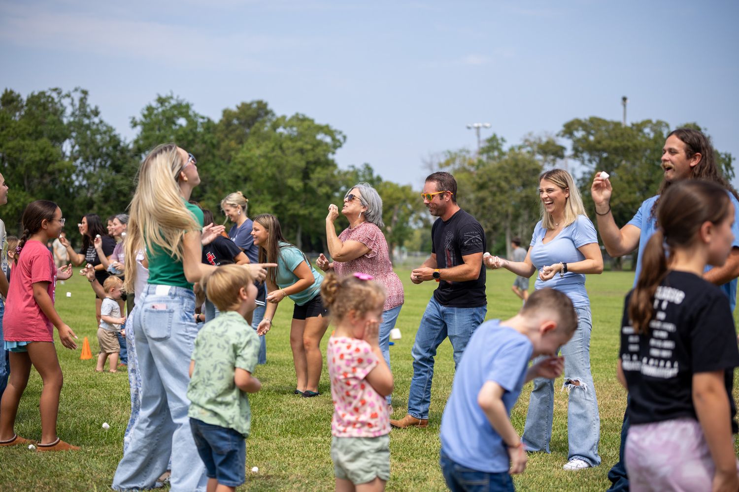 Families and children playing outdoors on a sunny green lawn at a community gathering event.