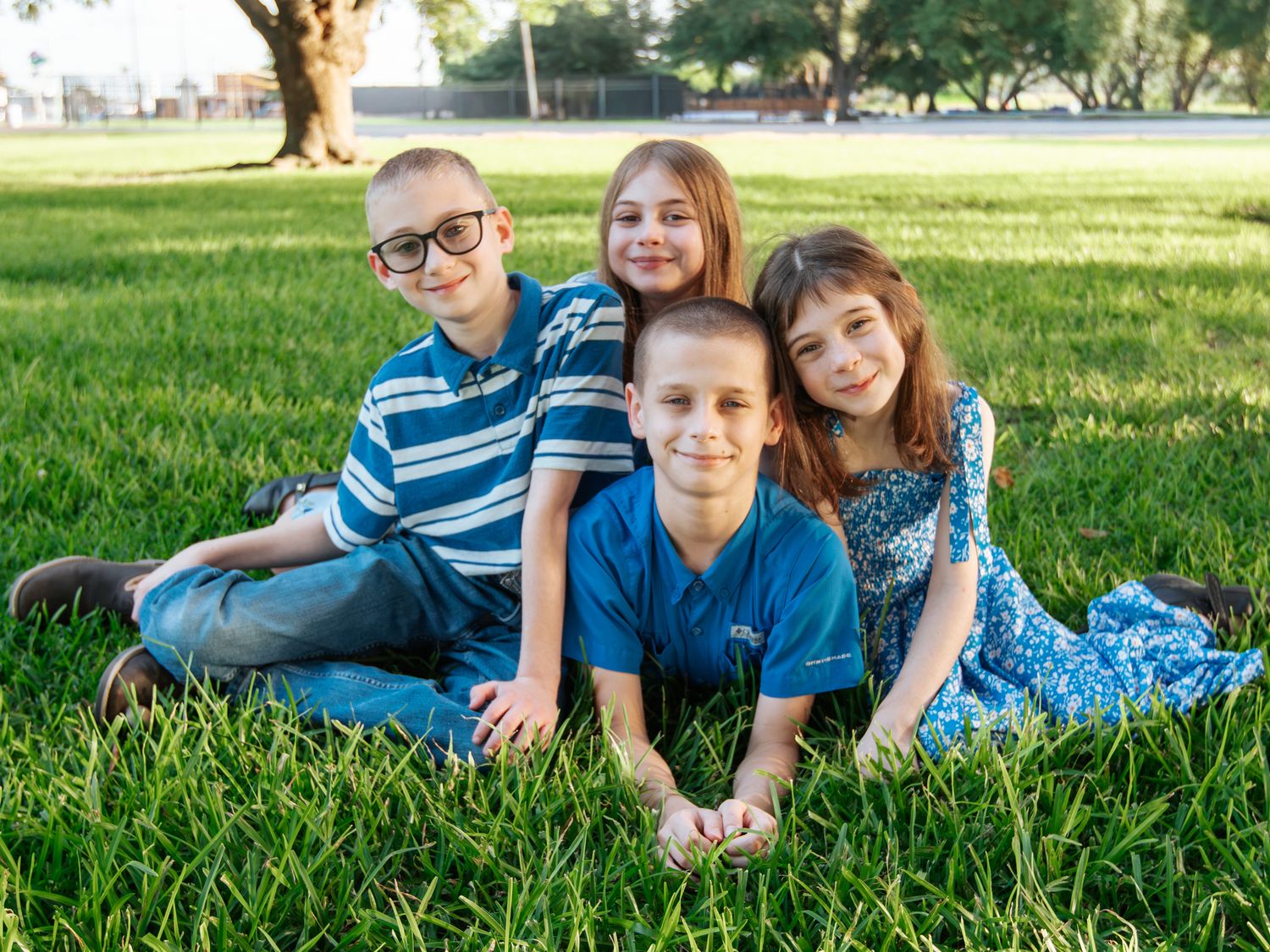 Four children smiling and posing together on green grass in a park during golden hour photography session.