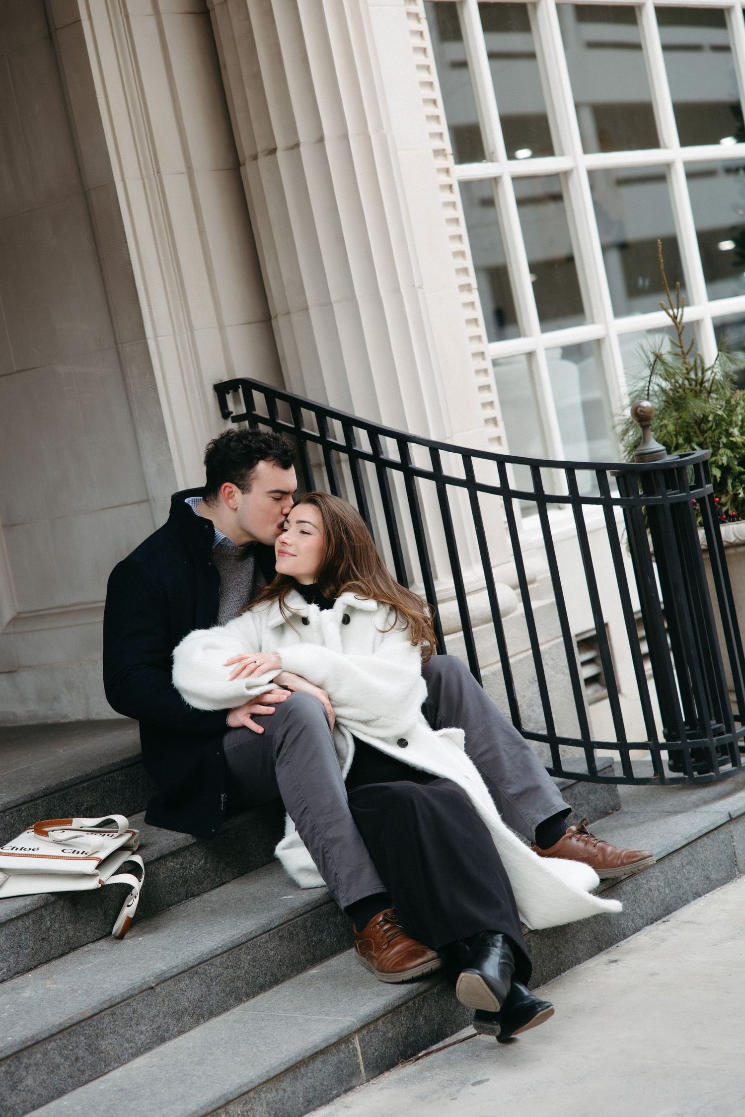 A romantic moment shared between two people sitting on stone steps outside a building with columns.